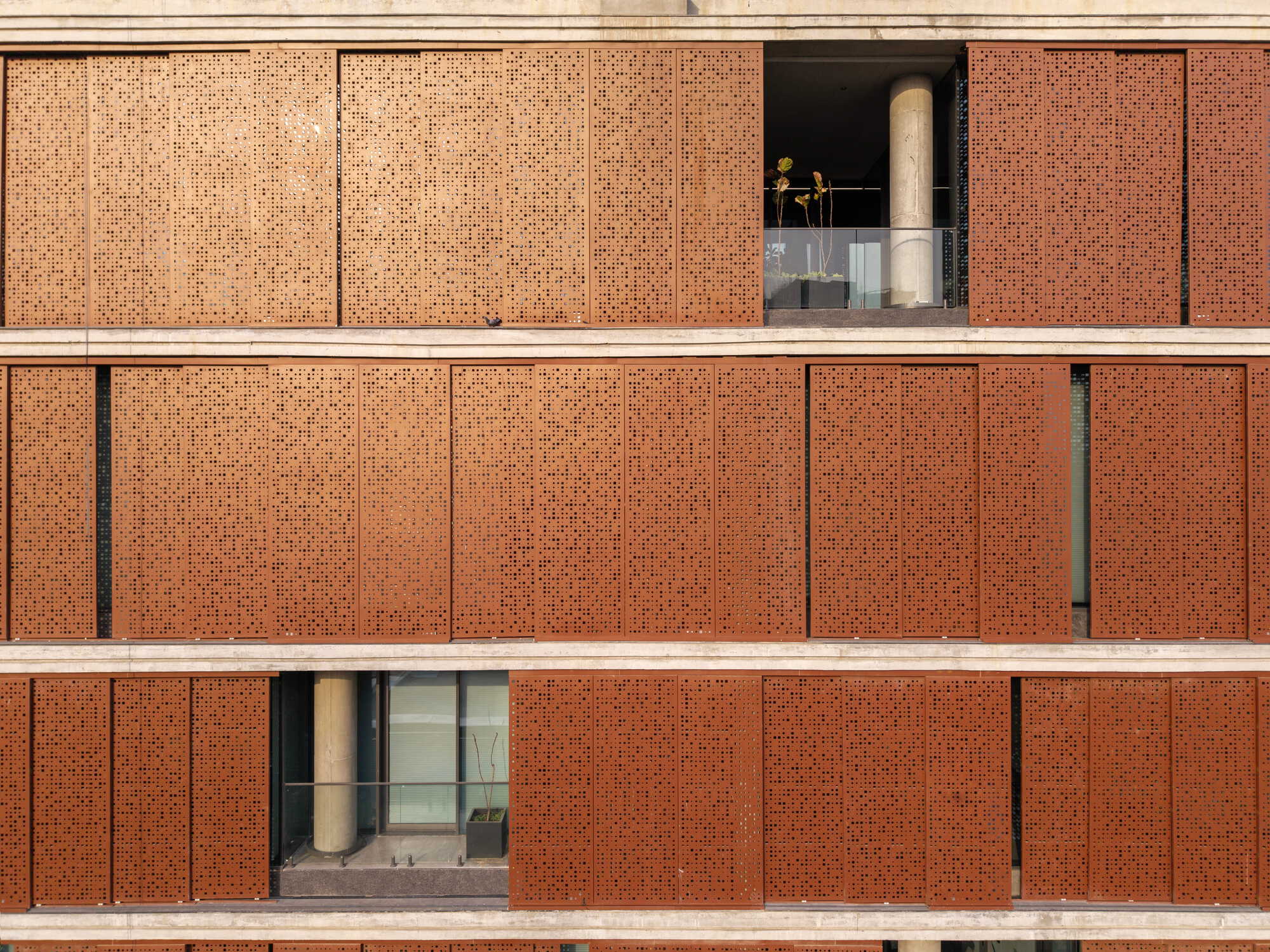 Front elevation of perforated brick facade with horizontal concrete bands and recessed balconies in warm light