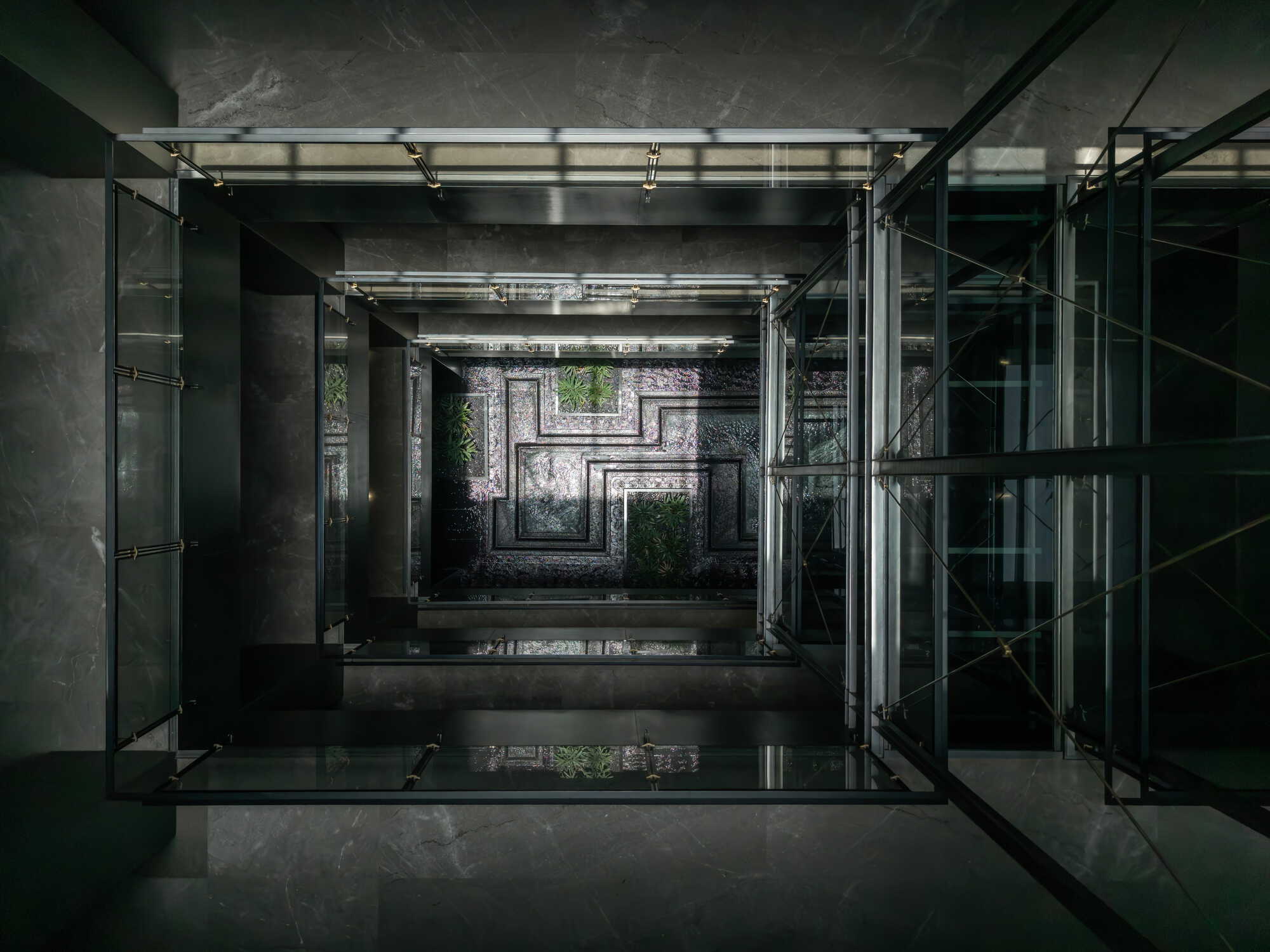View up through glass-roofed central atrium with concrete structure and cascading planted terraces