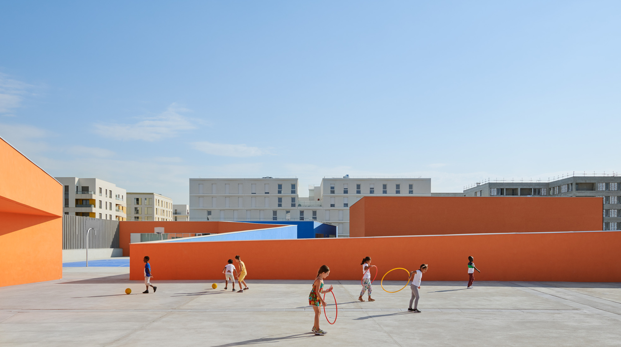 Children playing on the rooftop courtyard enclosed by tall orange walls and blue surfaces