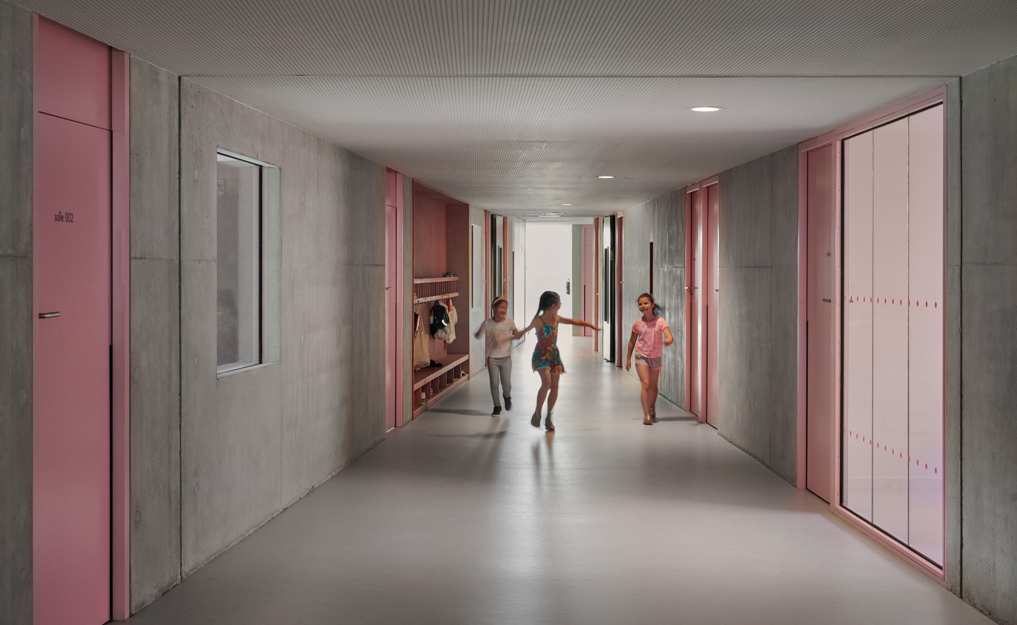 Corridor with pink doors and concrete walls where children run through the space