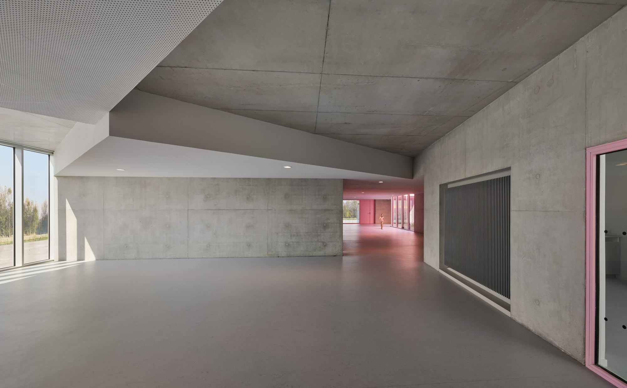 Concrete corridor with exposed ceiling and pink illuminated hallway receding into the distance