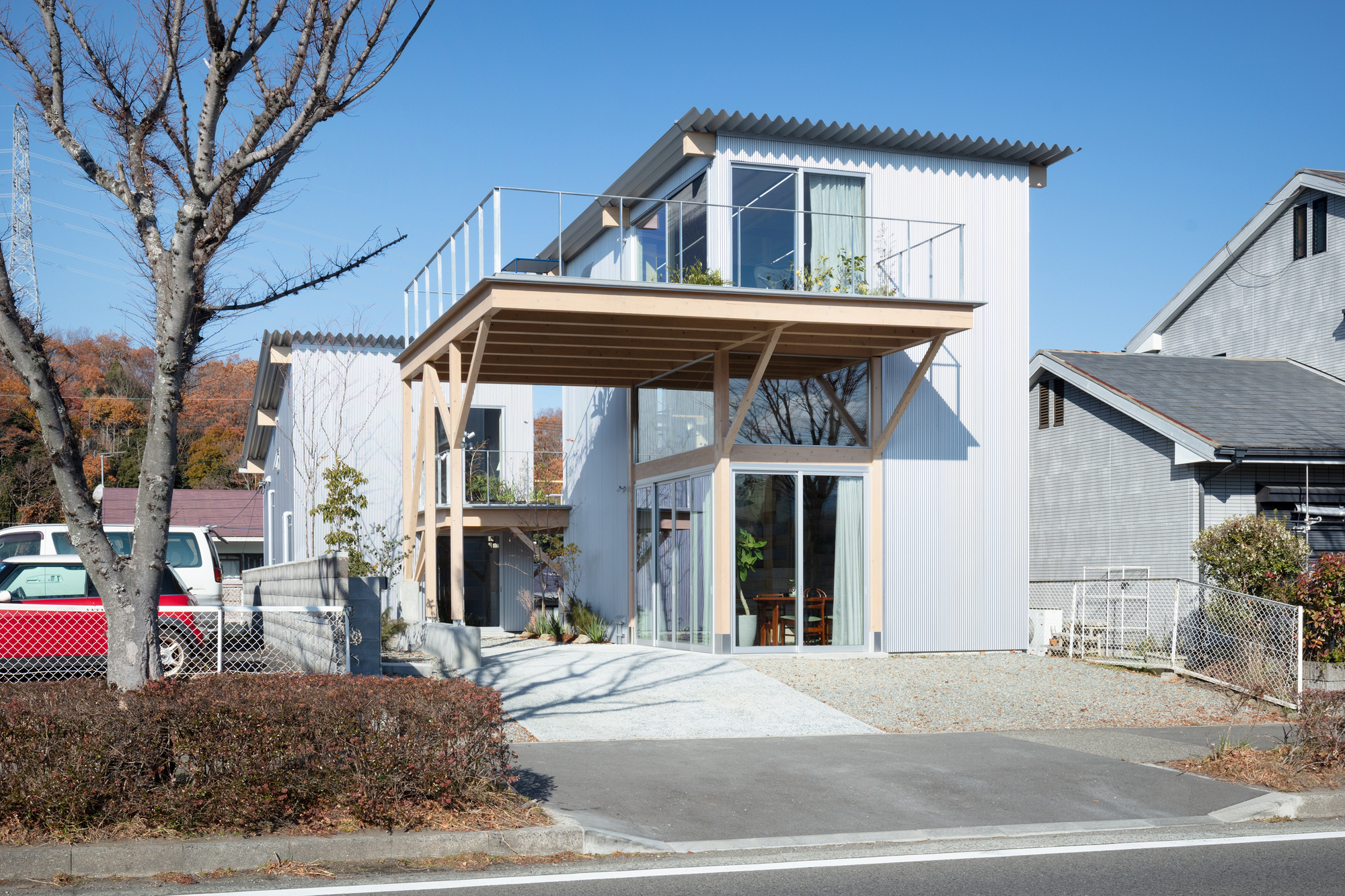 Street facade with exposed timber structure supporting an upper terrace and corrugated metal cladding in winter light