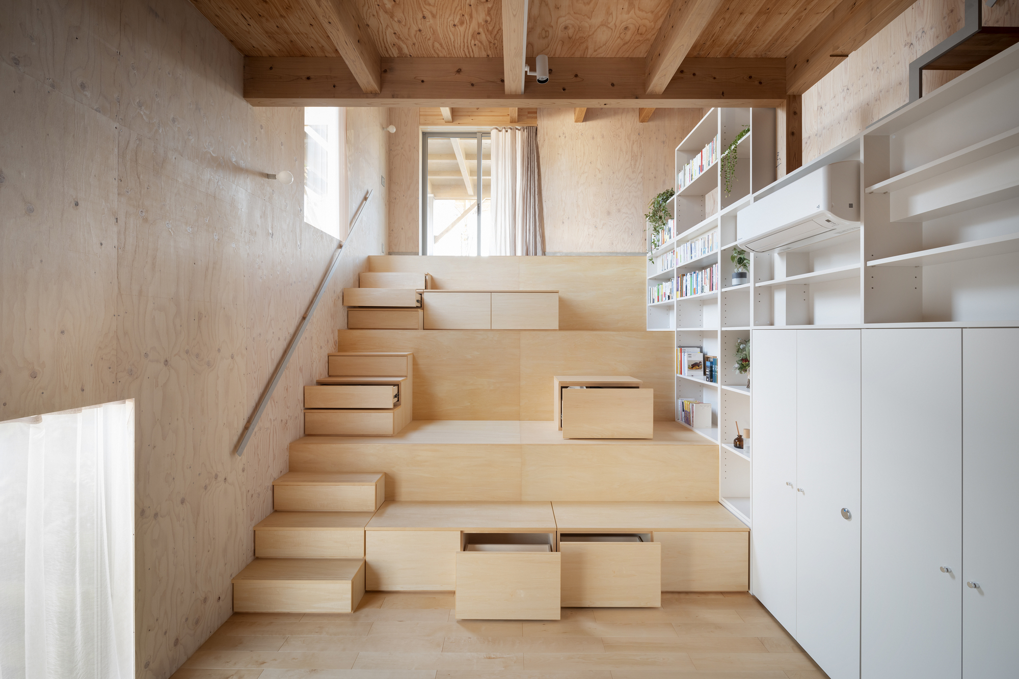 Wide plywood stair with integrated storage drawers and open shelving under exposed timber ceiling beams