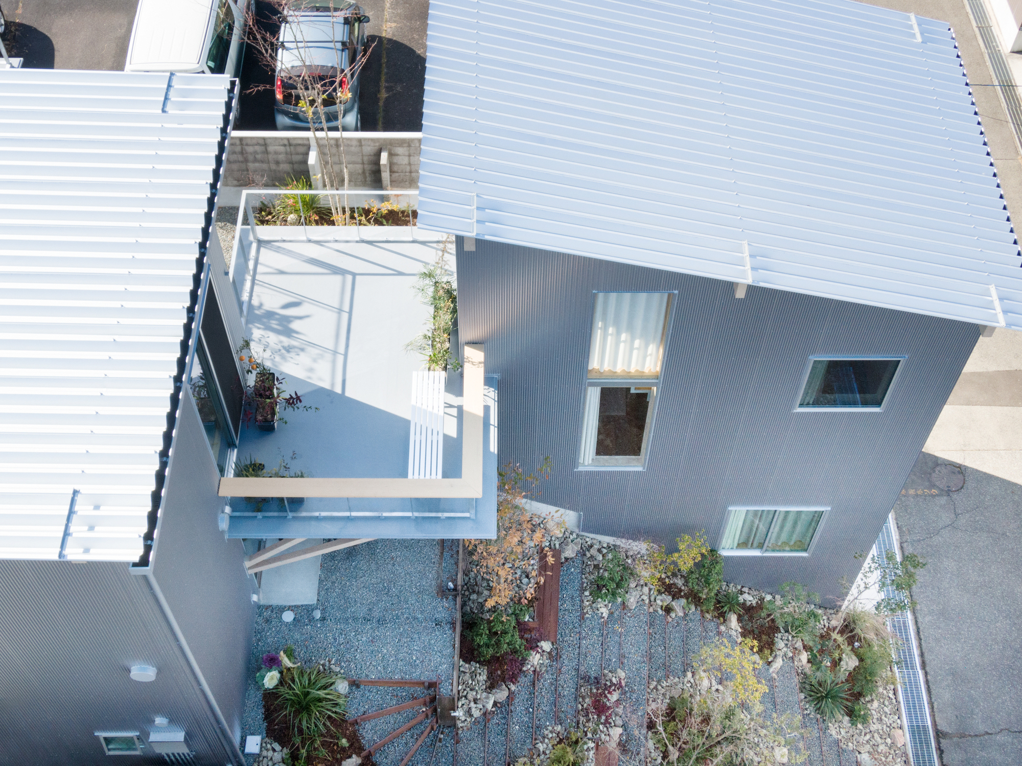 Aerial view of corrugated rooftop with planted gravel courtyard and scattered vegetation between metal-clad volumes