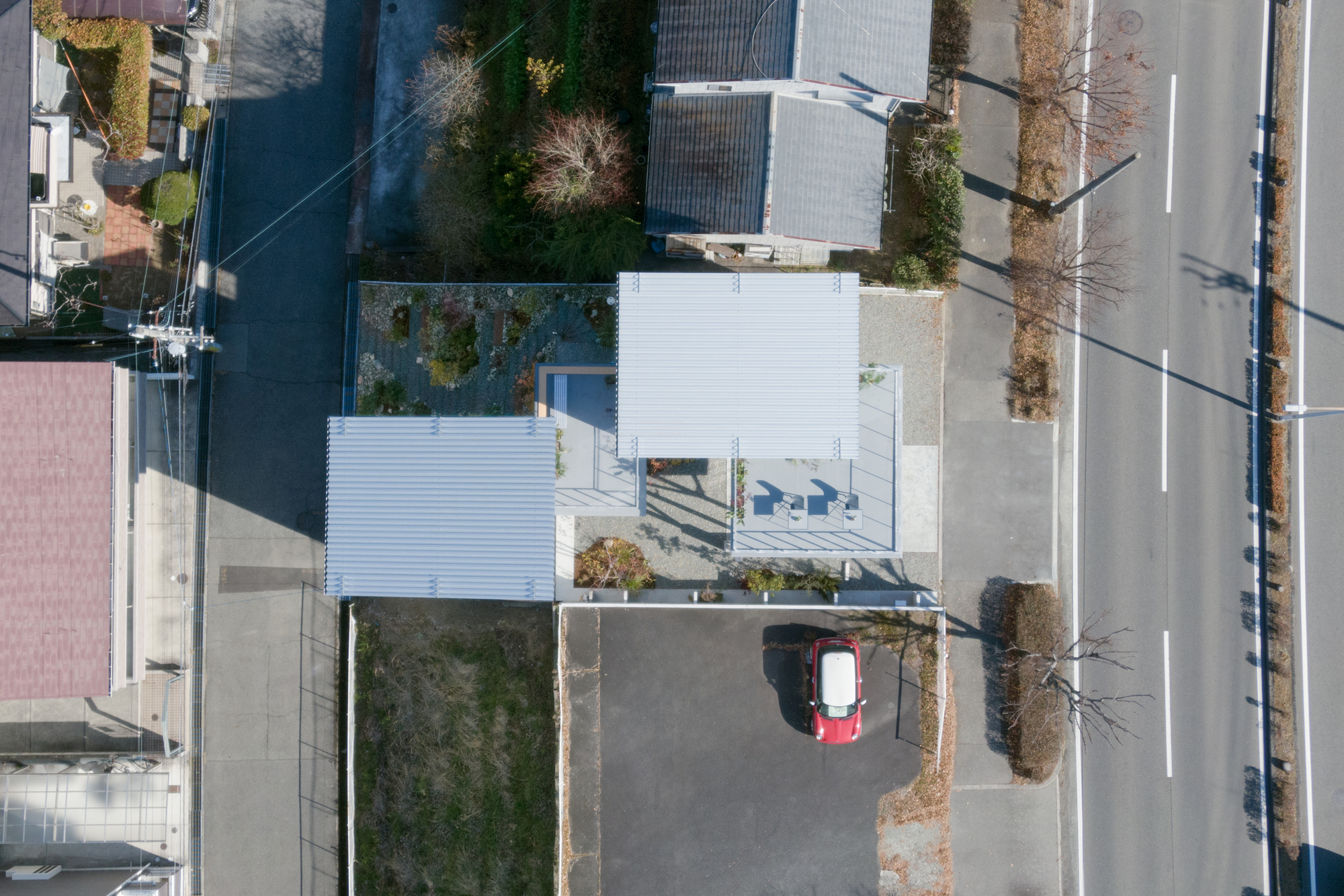Aerial view showing corrugated metal roofs and a small roof terrace with chairs beside a parked car