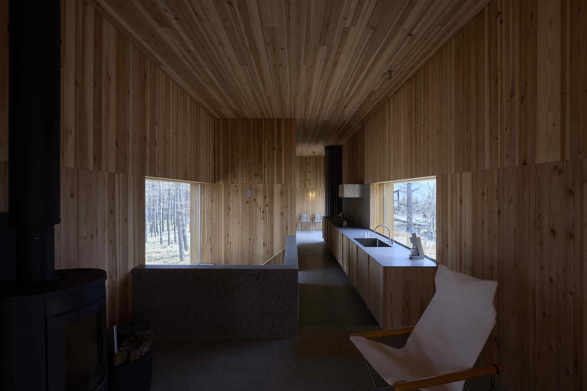 Kitchen and corridor with continuous timber surfaces and punched windows framing the winter forest