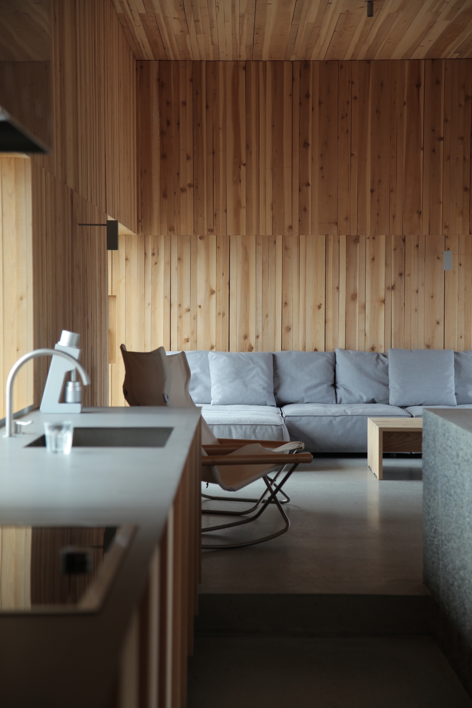 Living space with vertical timber walls, ceiling, and grey sofa in natural light