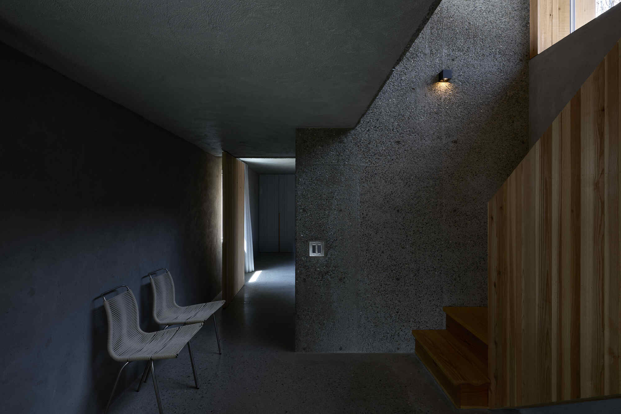 Dark textured concrete corridor with timber partition and recessed wall sconce