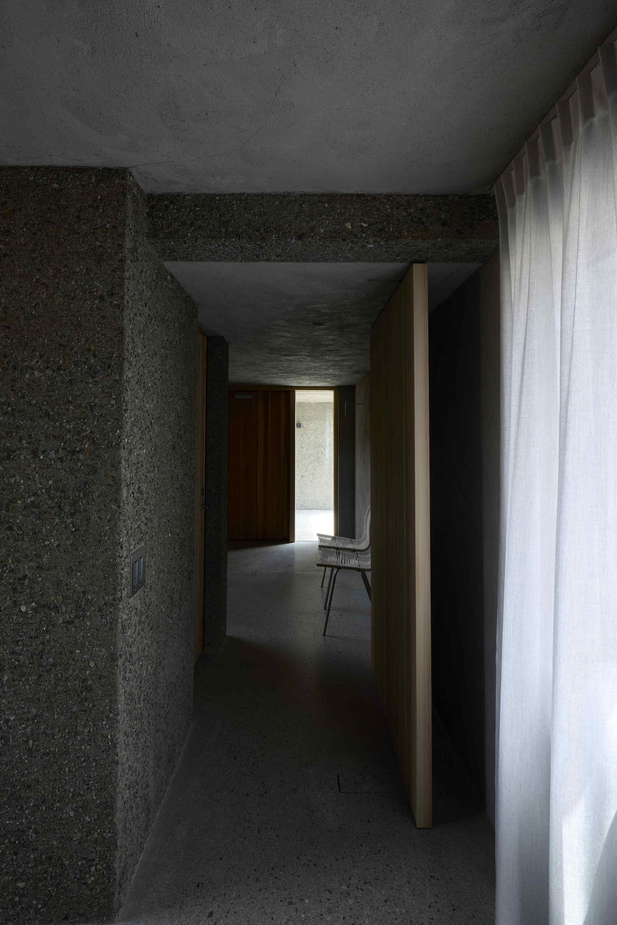 Concrete hallway with timber door jamb and chair silhouetted in daylit opening
