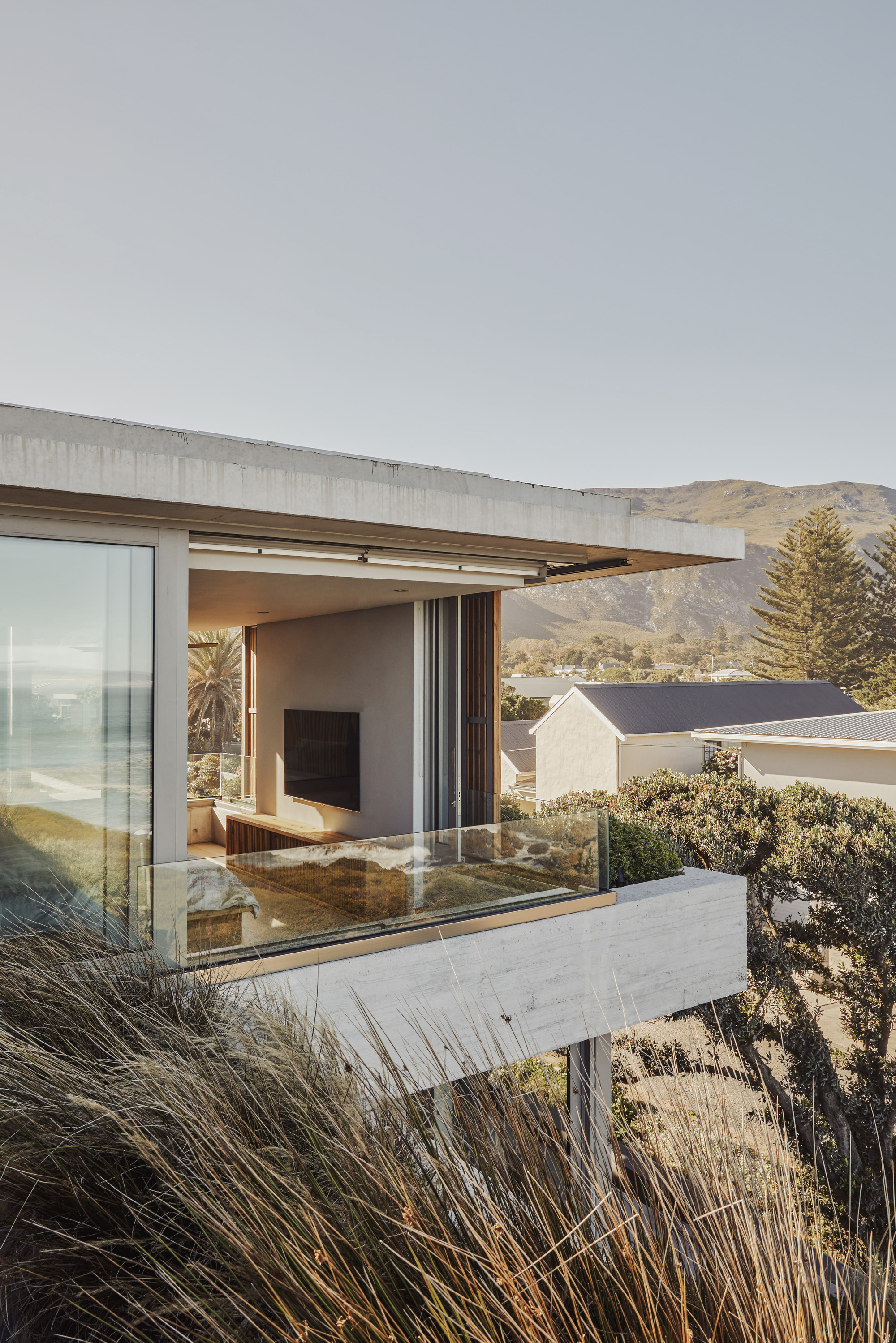 Cantilevered concrete terrace with sliding glass doors opening to a living room, framed by coastal grasses