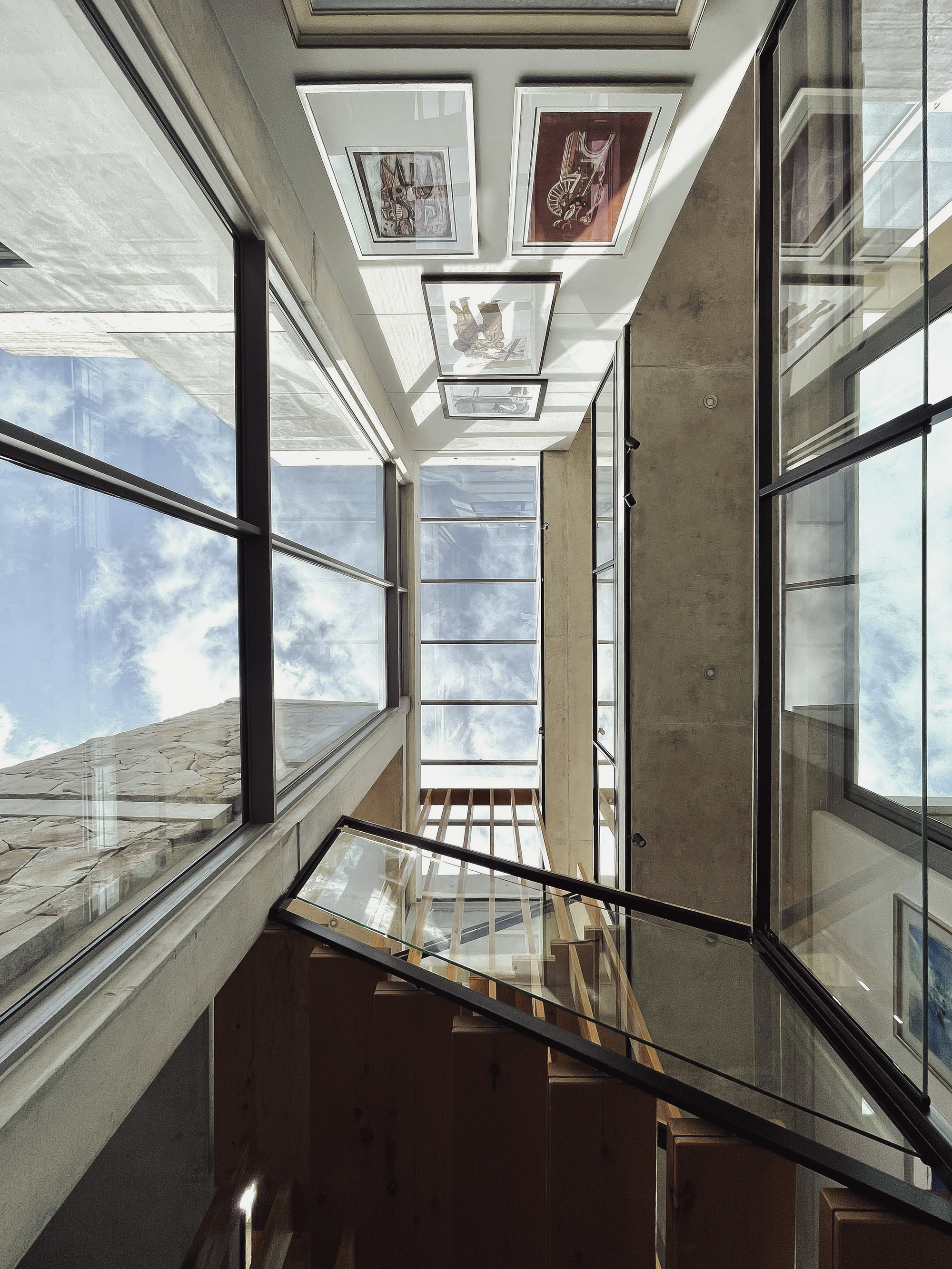 Upward view of a multi-story stairwell with skylights, timber treads and glass balustrades under blue sky