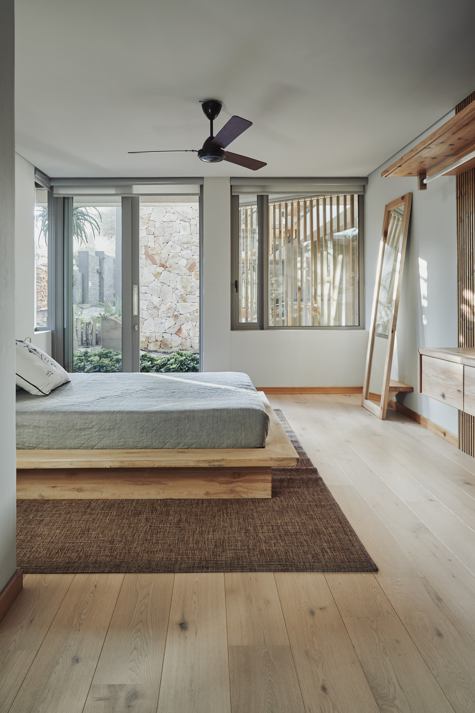 Bedroom with timber platform bed, ceiling fan and glass doors opening to a stone courtyard wall