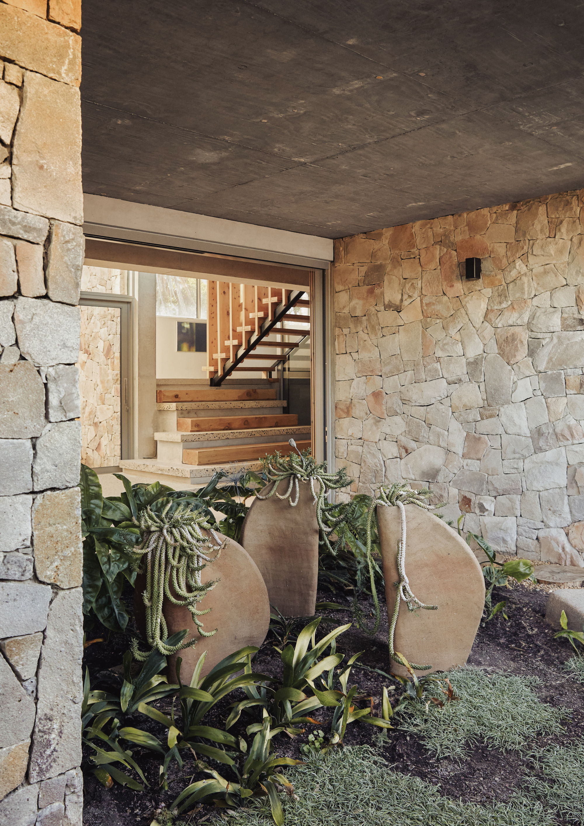 Entry courtyard with stone wall, planted bed with curved steel planters and cascading succulents