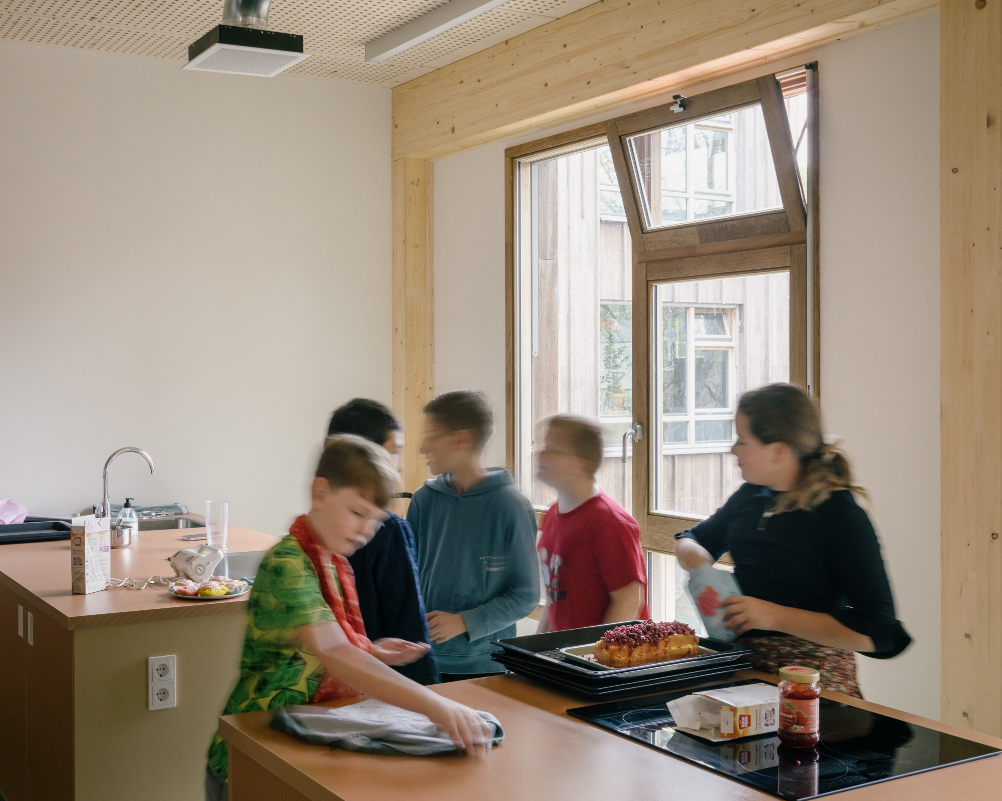 Group of children preparing food at a counter with sink and cooktop by a window