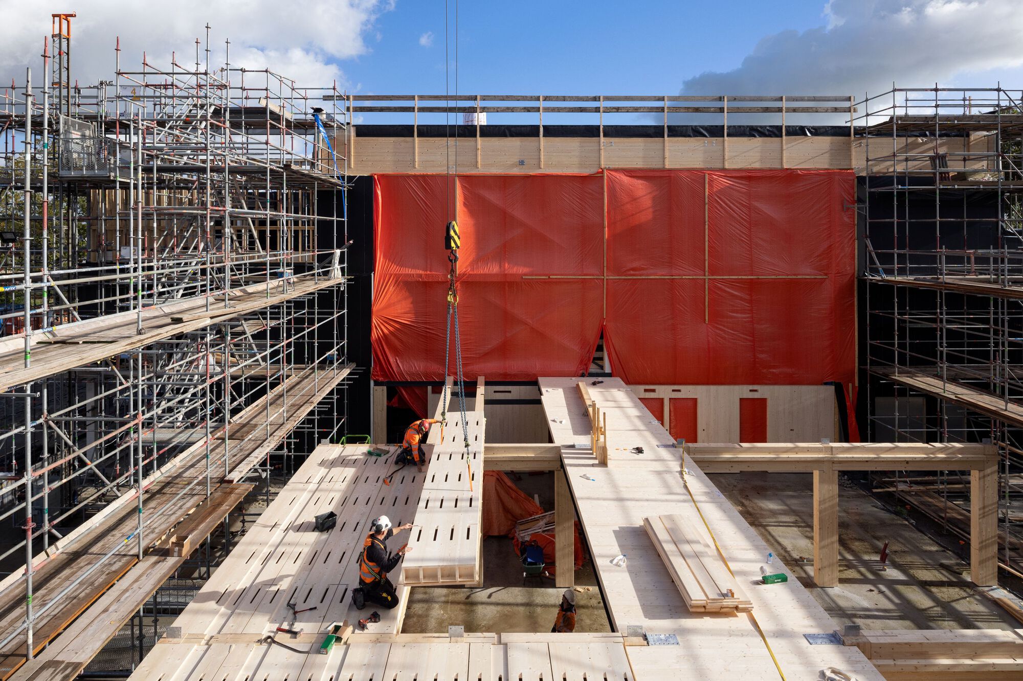 Construction site view showing red weatherproofing membrane and scaffolding surrounding timber structural frame