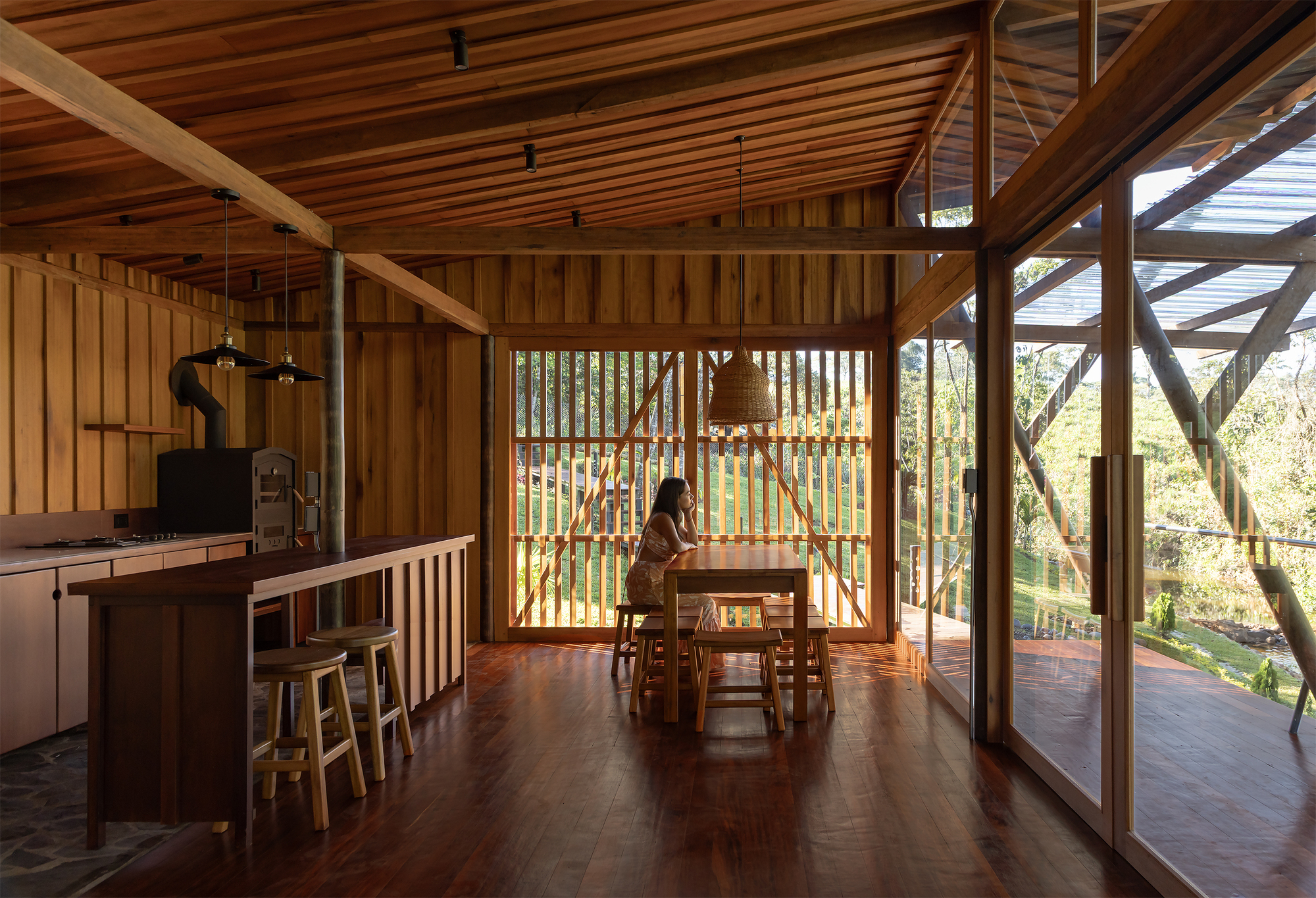 Open-plan interior with slatted timber ceiling, vertical bamboo screen and person seated at dining table