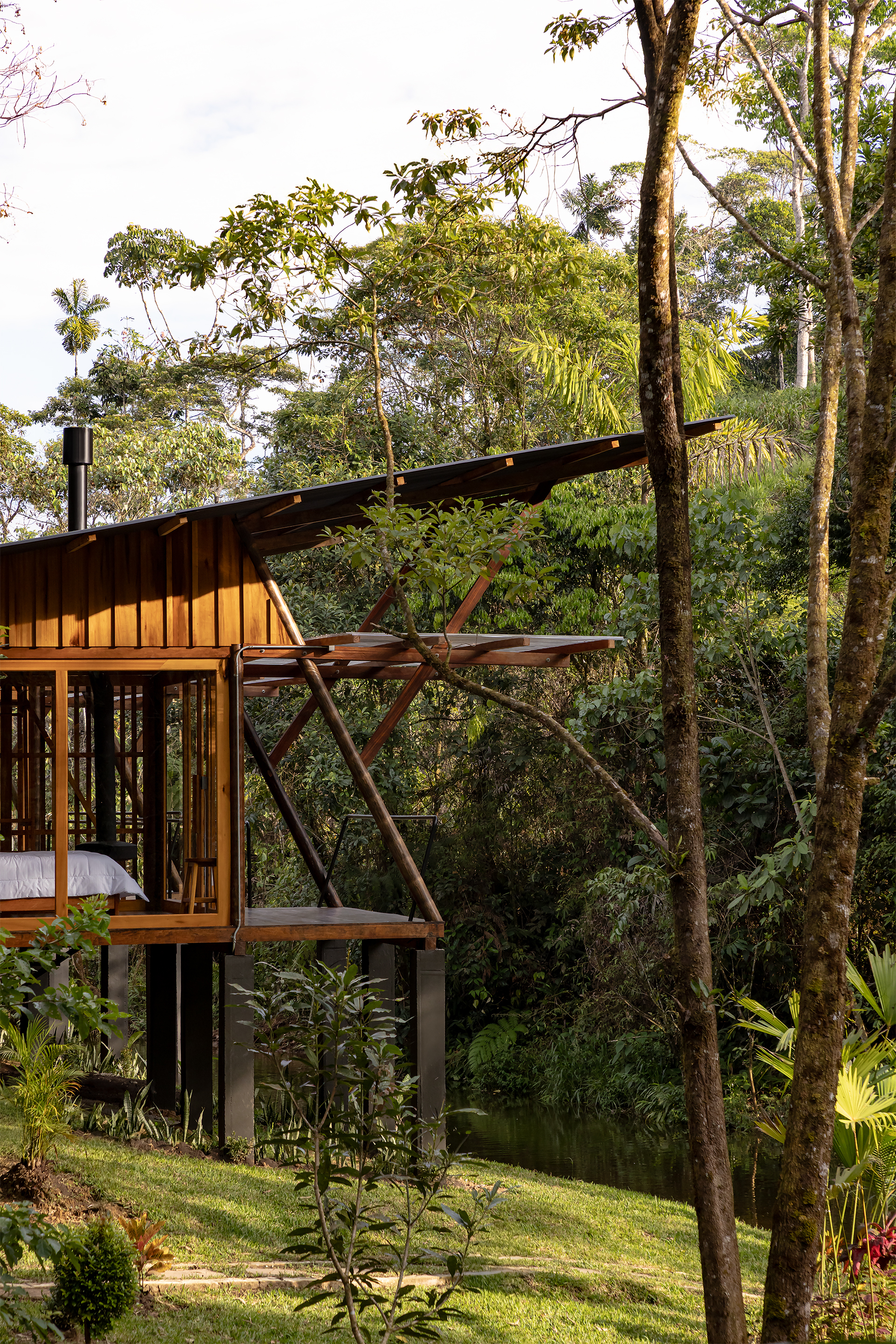 Corner view showing diagonal timber supports and cantilevered roof section above sloped lawn and trees