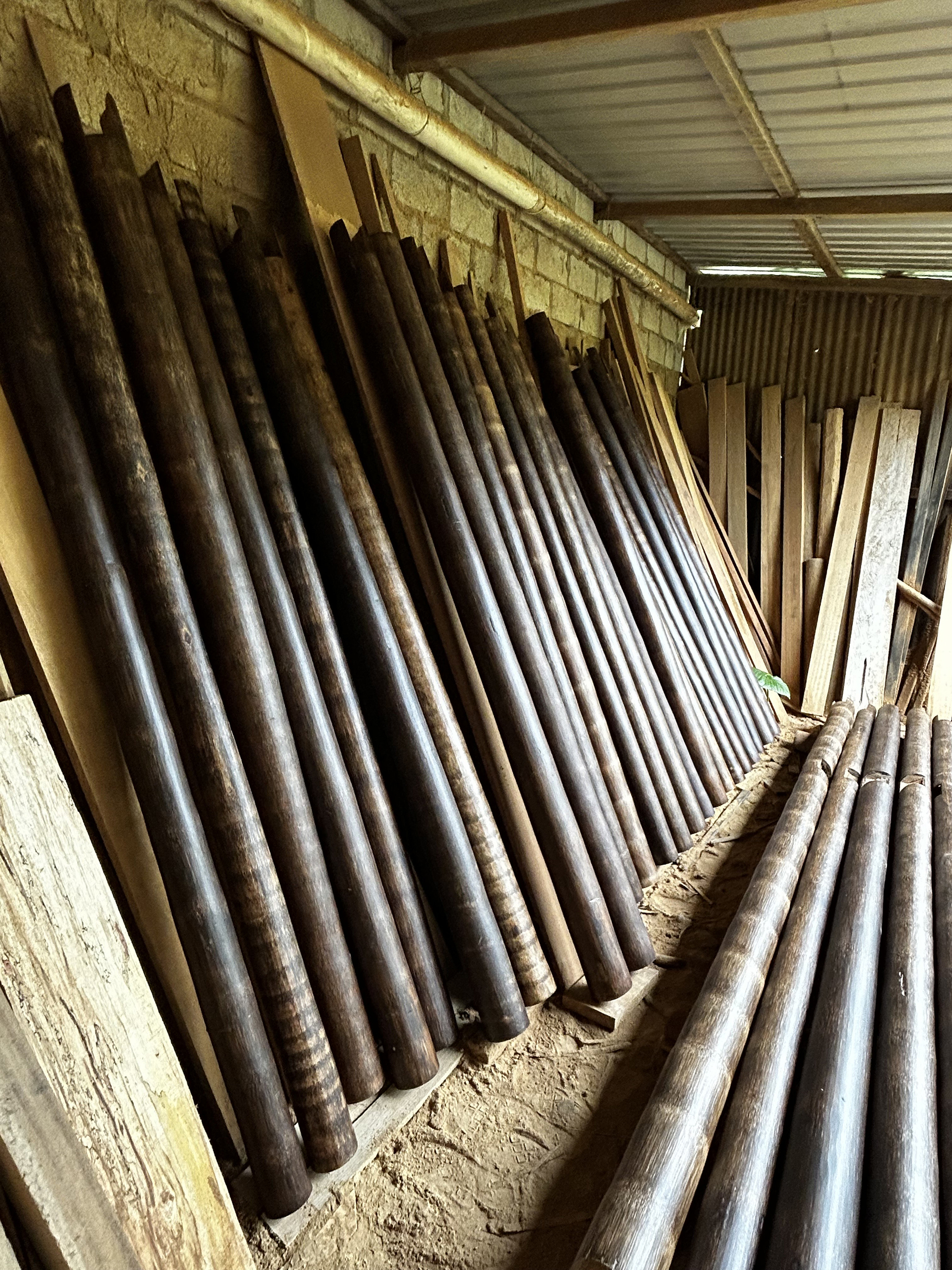 Storage of bamboo poles leaning against an earthen wall under a corrugated metal roof