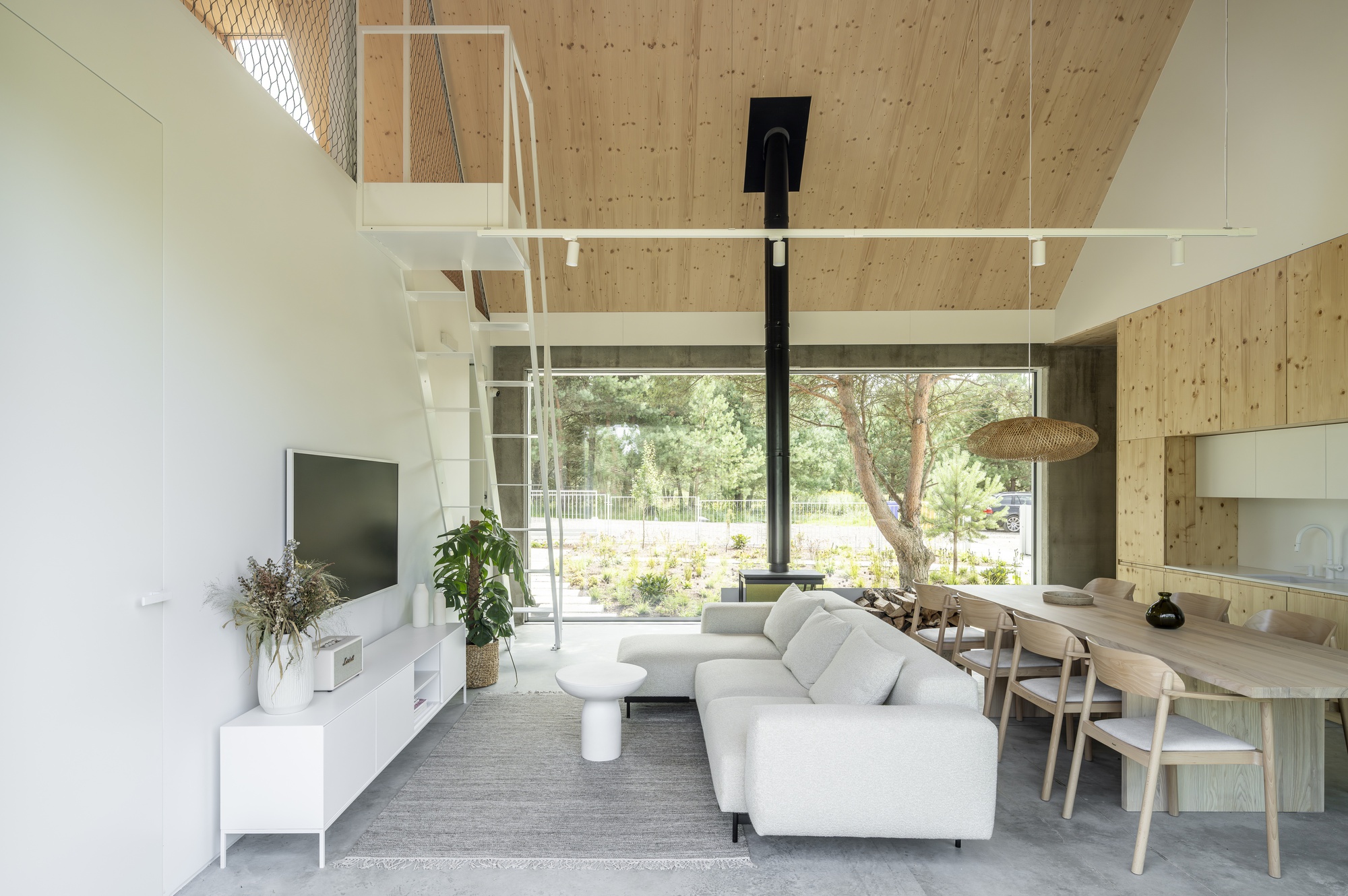 Open-plan living space with exposed plywood ceiling and white metal stair leading to upper level