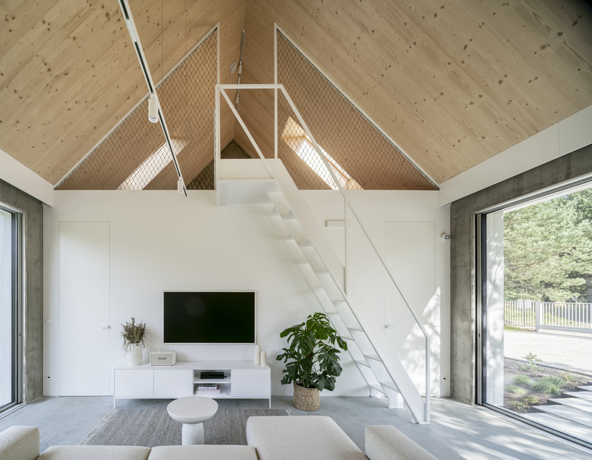 White metal stair beneath the vaulted plywood ceiling with mesh safety panels catching sunlight