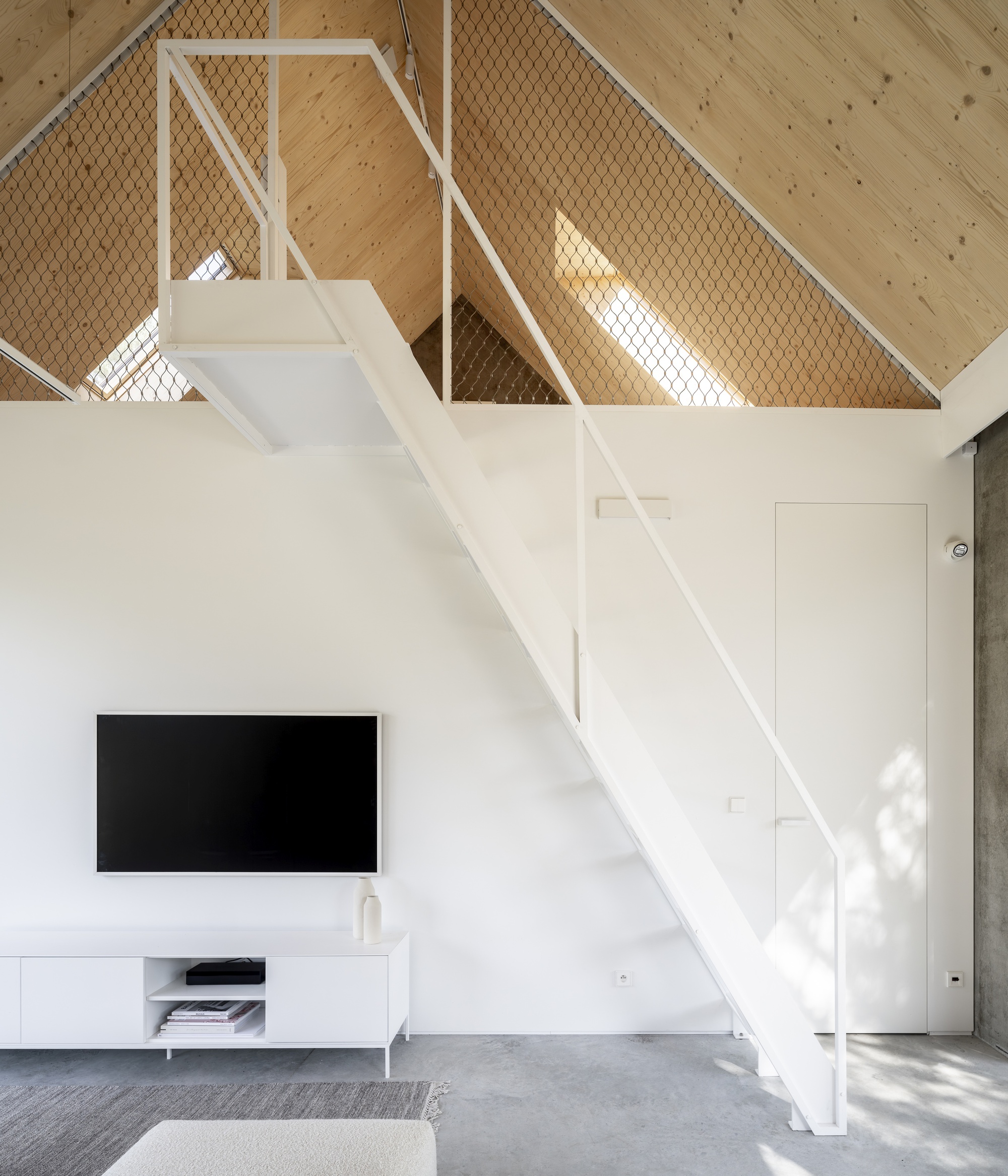 White steel staircase ascending to mezzanine level with wire mesh balustrade panels and timber ceiling