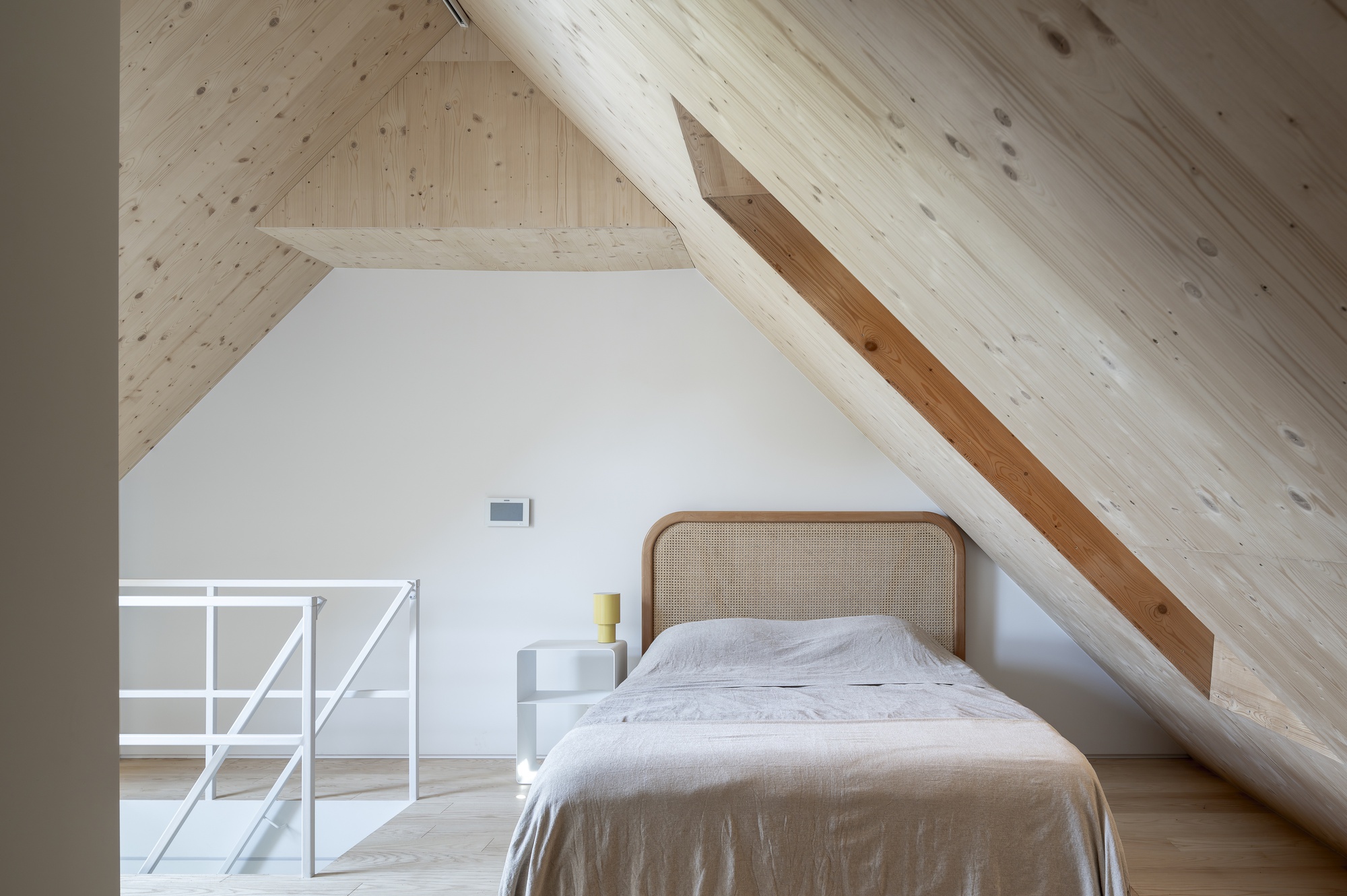Bedroom beneath an angled timber plank ceiling with exposed structural beam running diagonally overhead