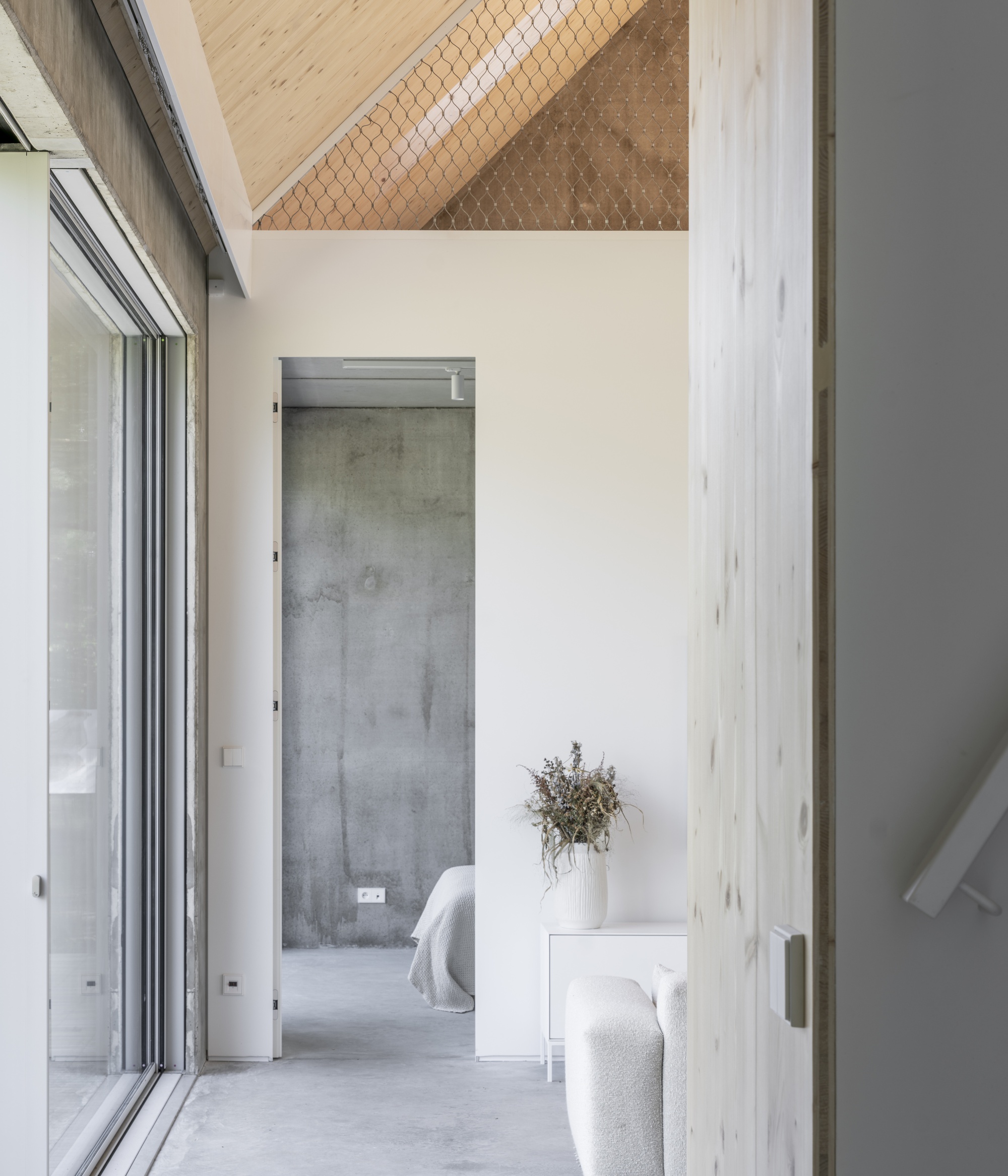 Hallway with polished concrete floor looking through to a bedroom framed by light timber columns