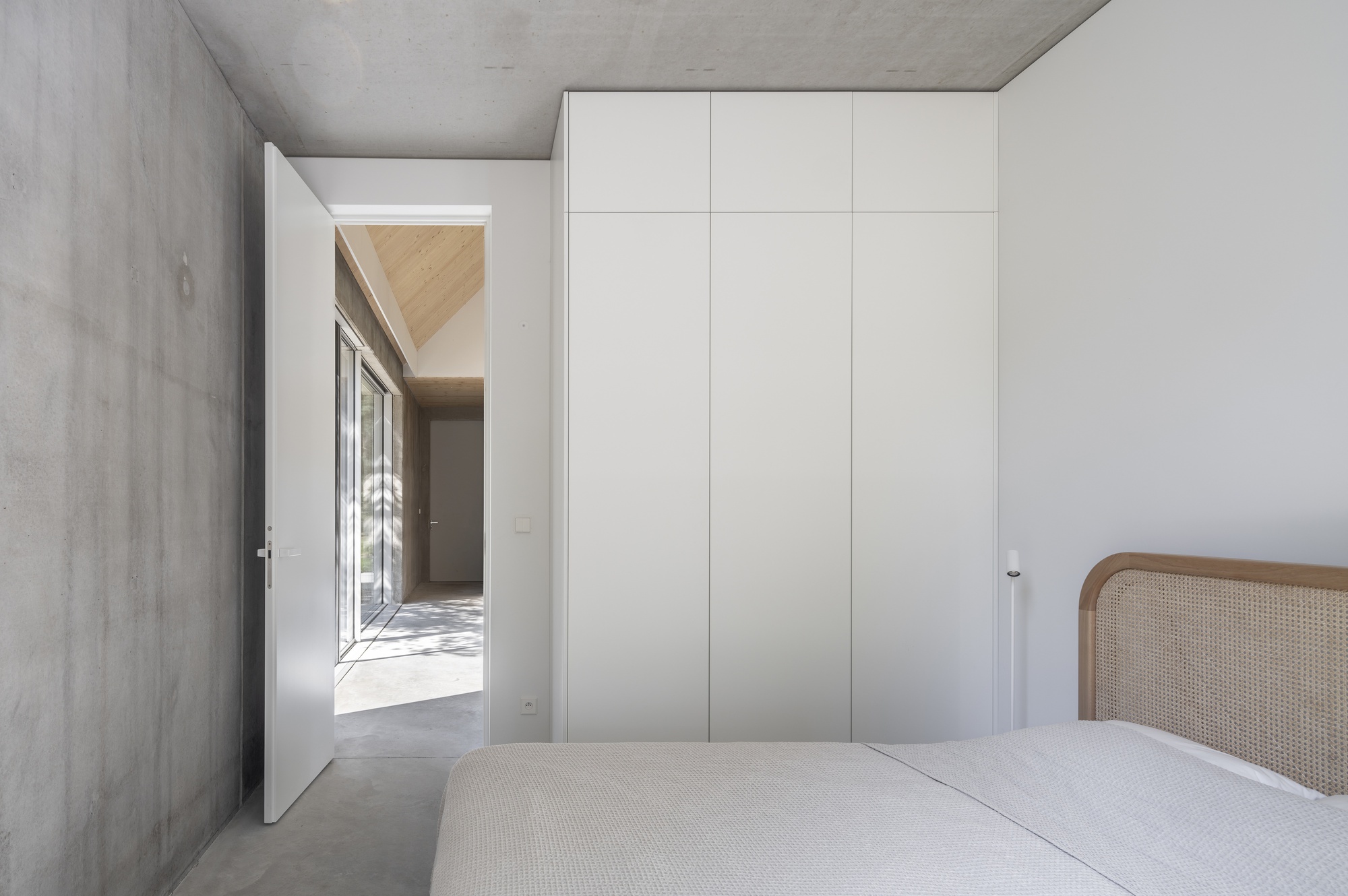 Bedroom with exposed concrete walls and ceiling featuring a full-height white storage cabinet
