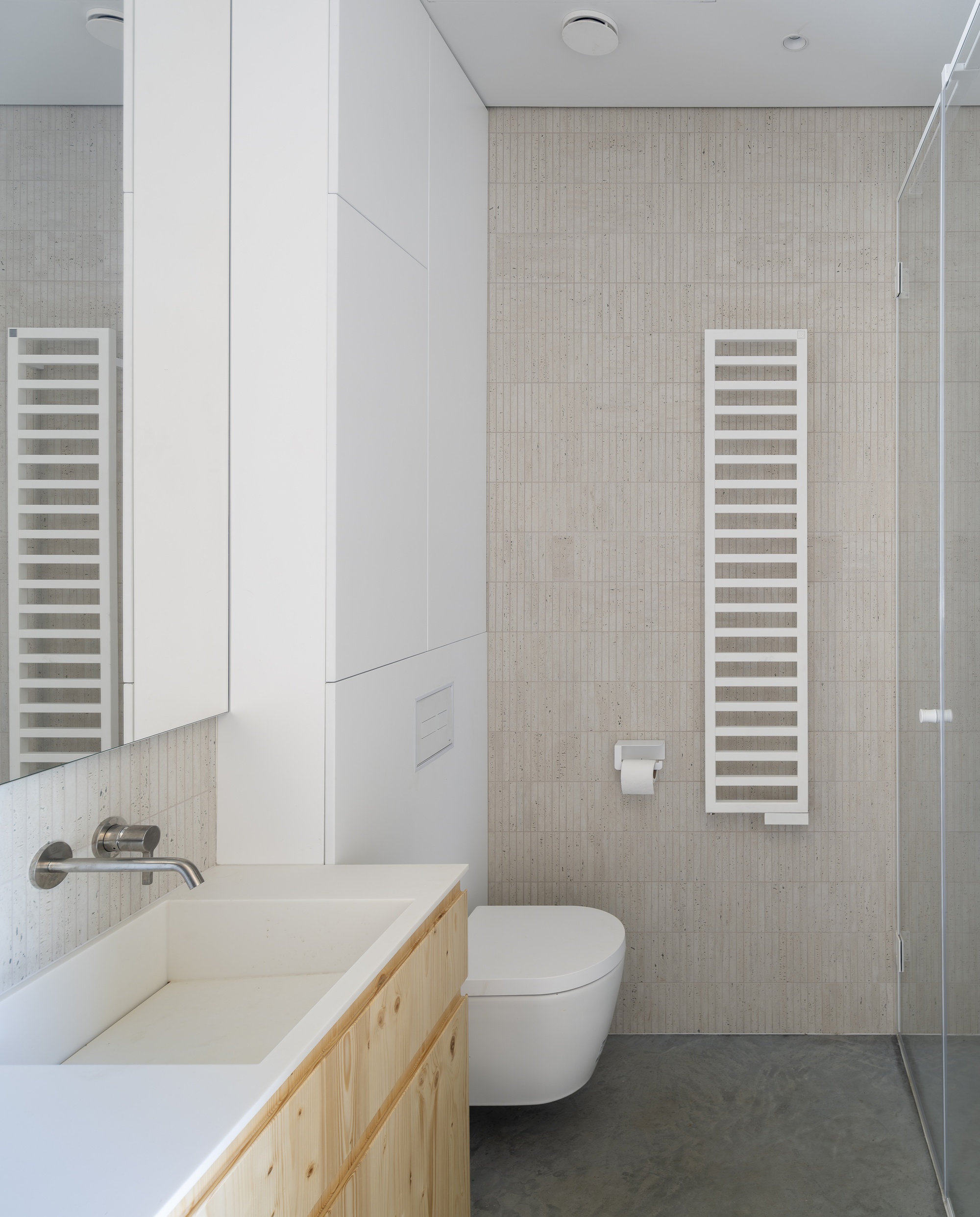 Bathroom interior with pale wood vanity, white towel radiators, and vertical tile accent wall