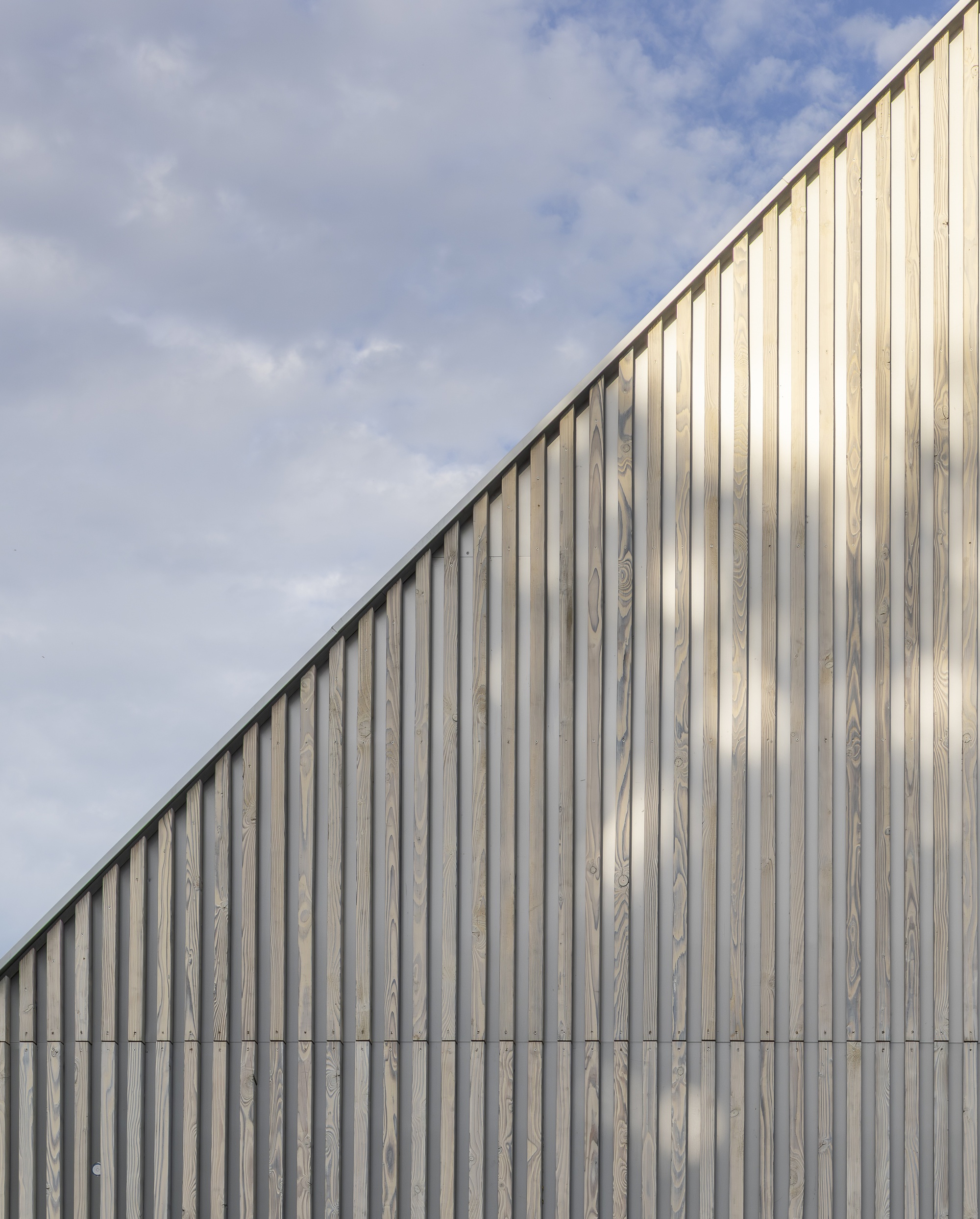 Vertical timber cladding facade sloping upward against a cloudy sky