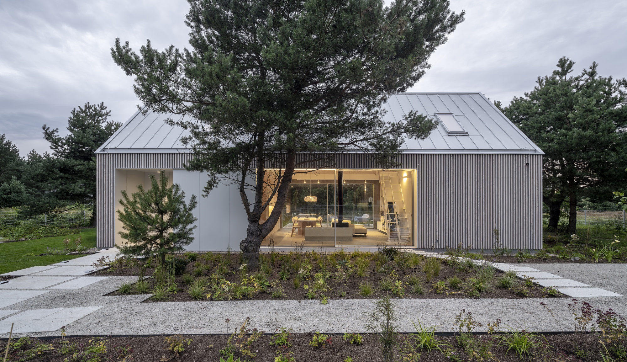 Twin gabled volumes clad in vertical timber with glazed living space and surrounding planted beds