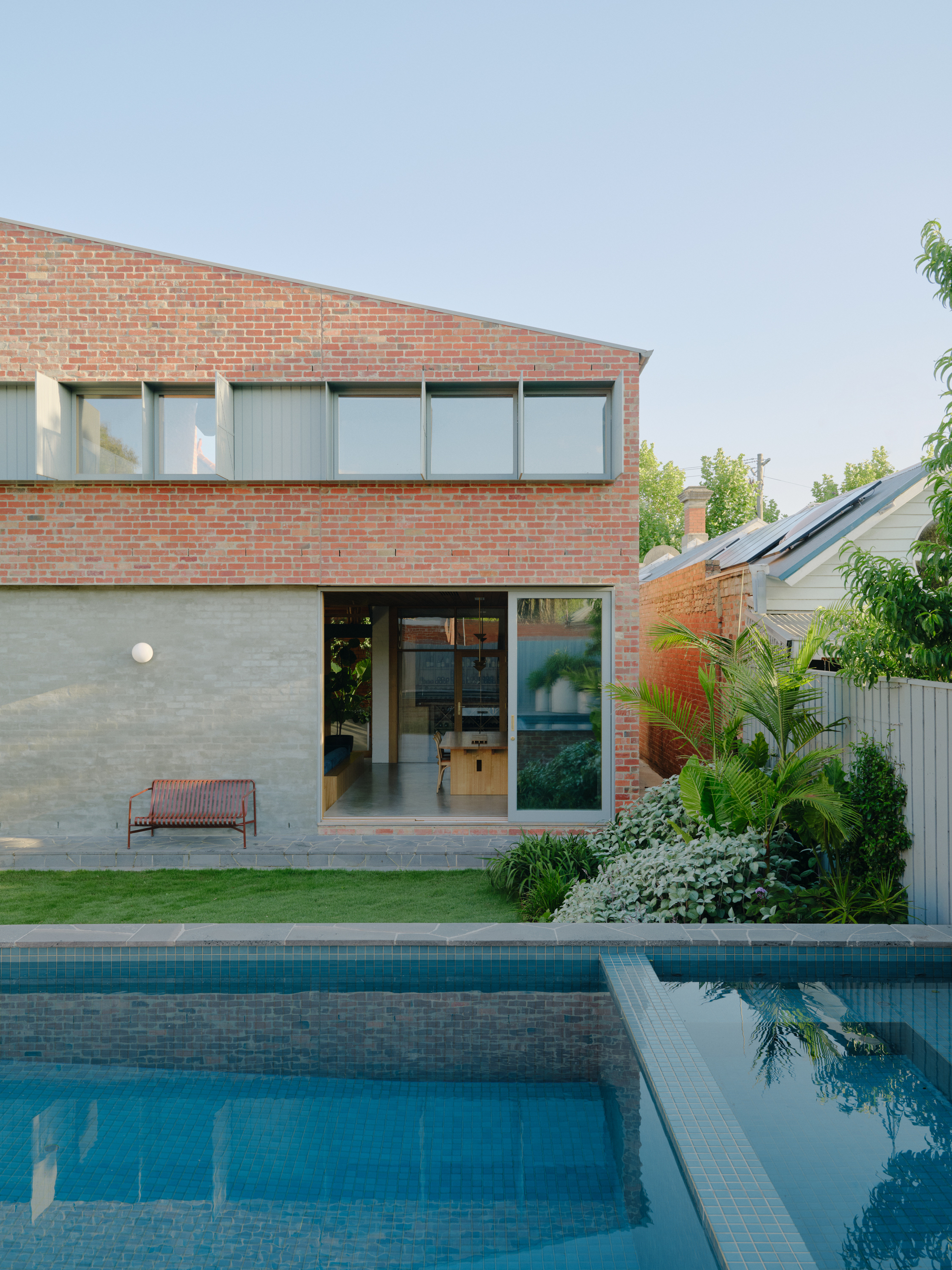 Two-storey brick addition with ribbon windows overlooking a swimming pool and lawn at dusk