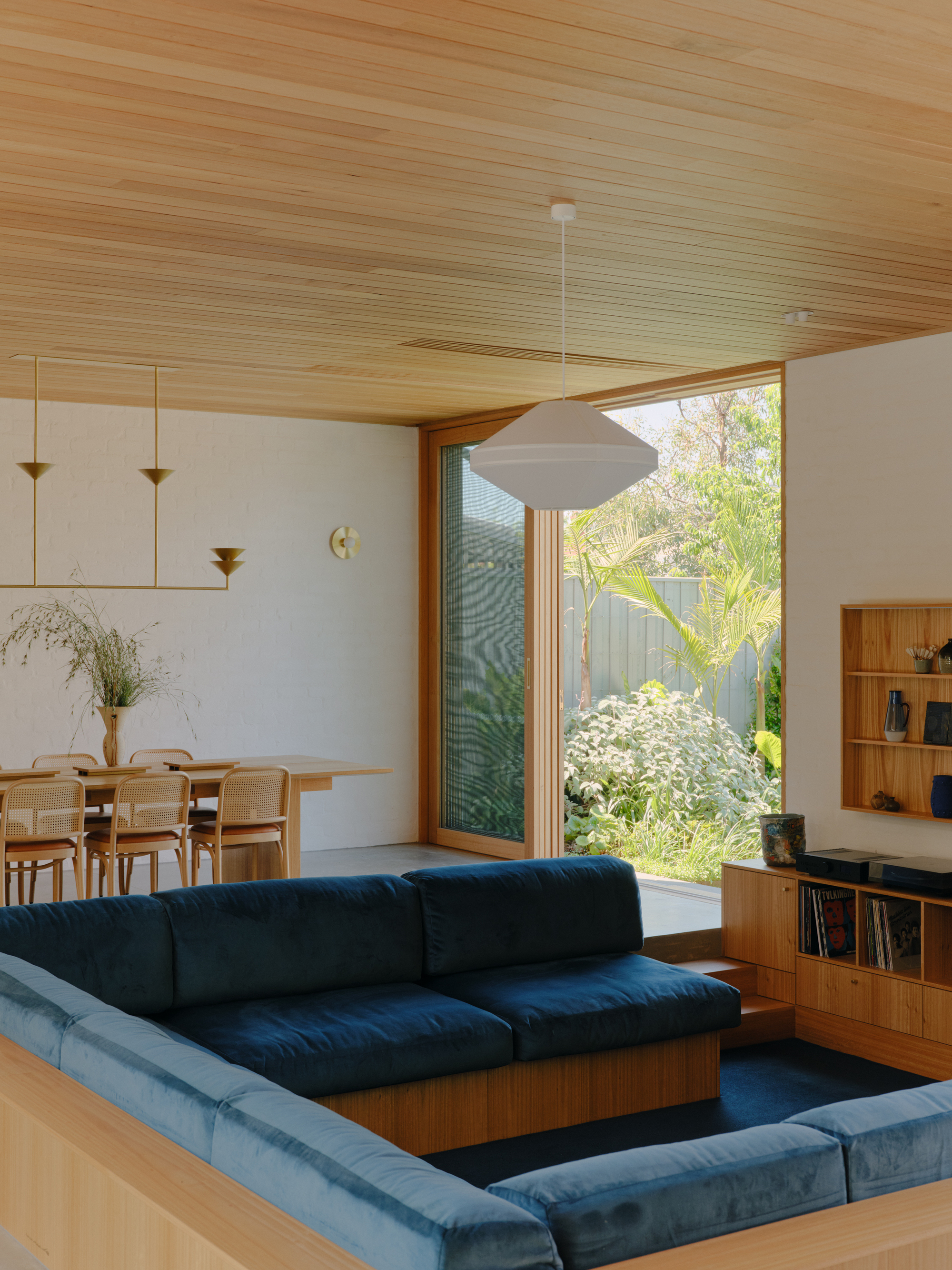 Living room with timber-lined ceiling and glazed doors opening to a planted courtyard