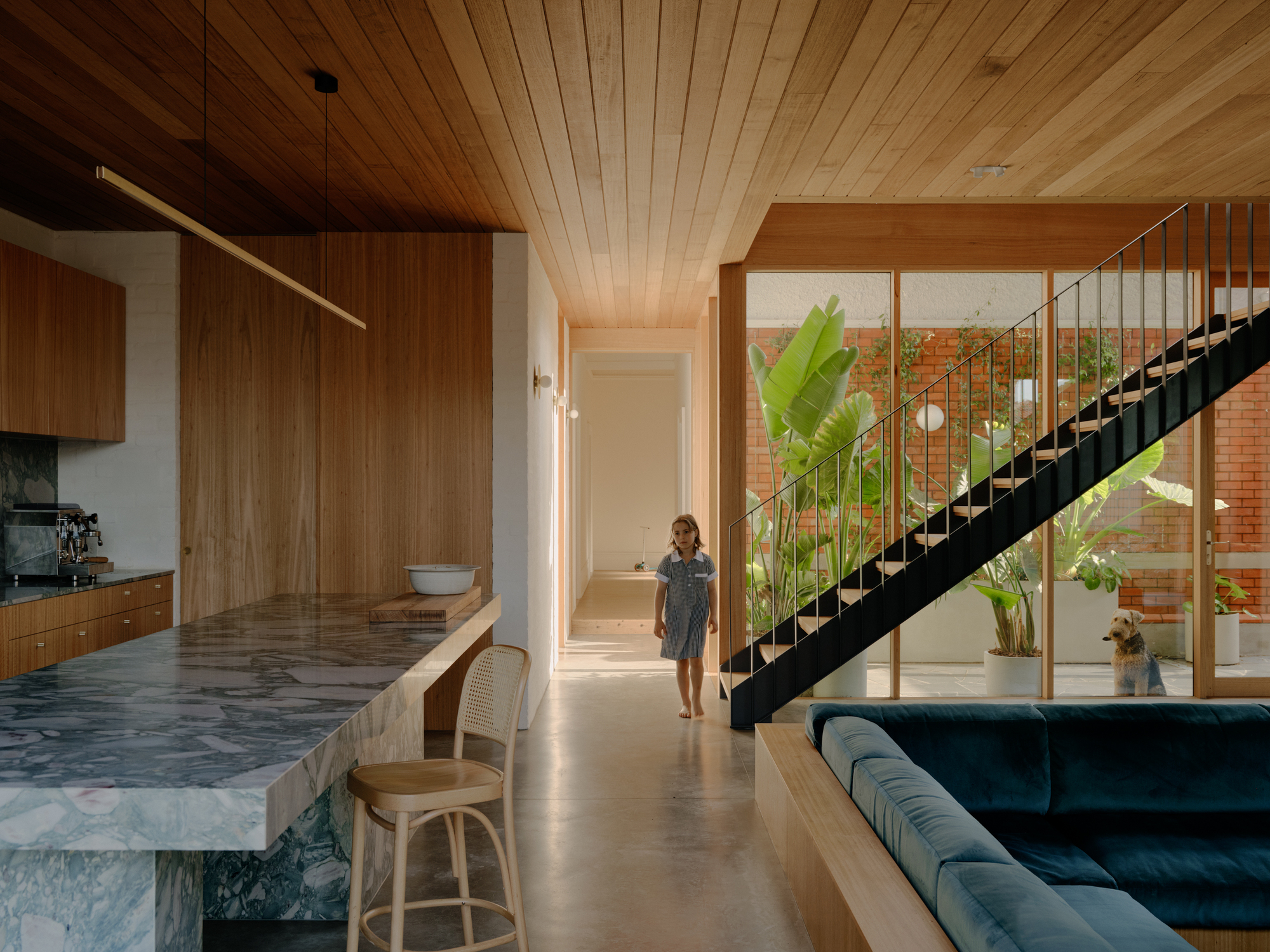 Open-plan interior with black steel staircase ascending past full-height glazing and a person walking