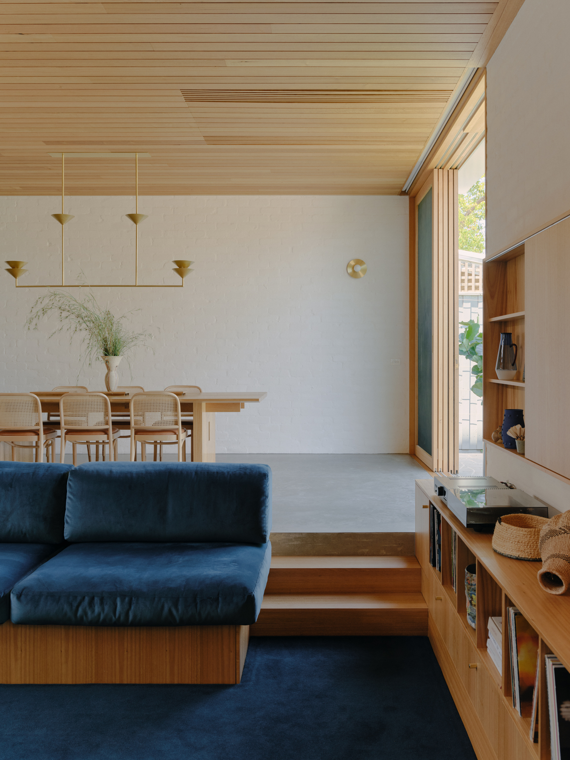 Open-plan living space with timber-lined ceiling, blue sofa, dining area and folding glass doors to courtyard