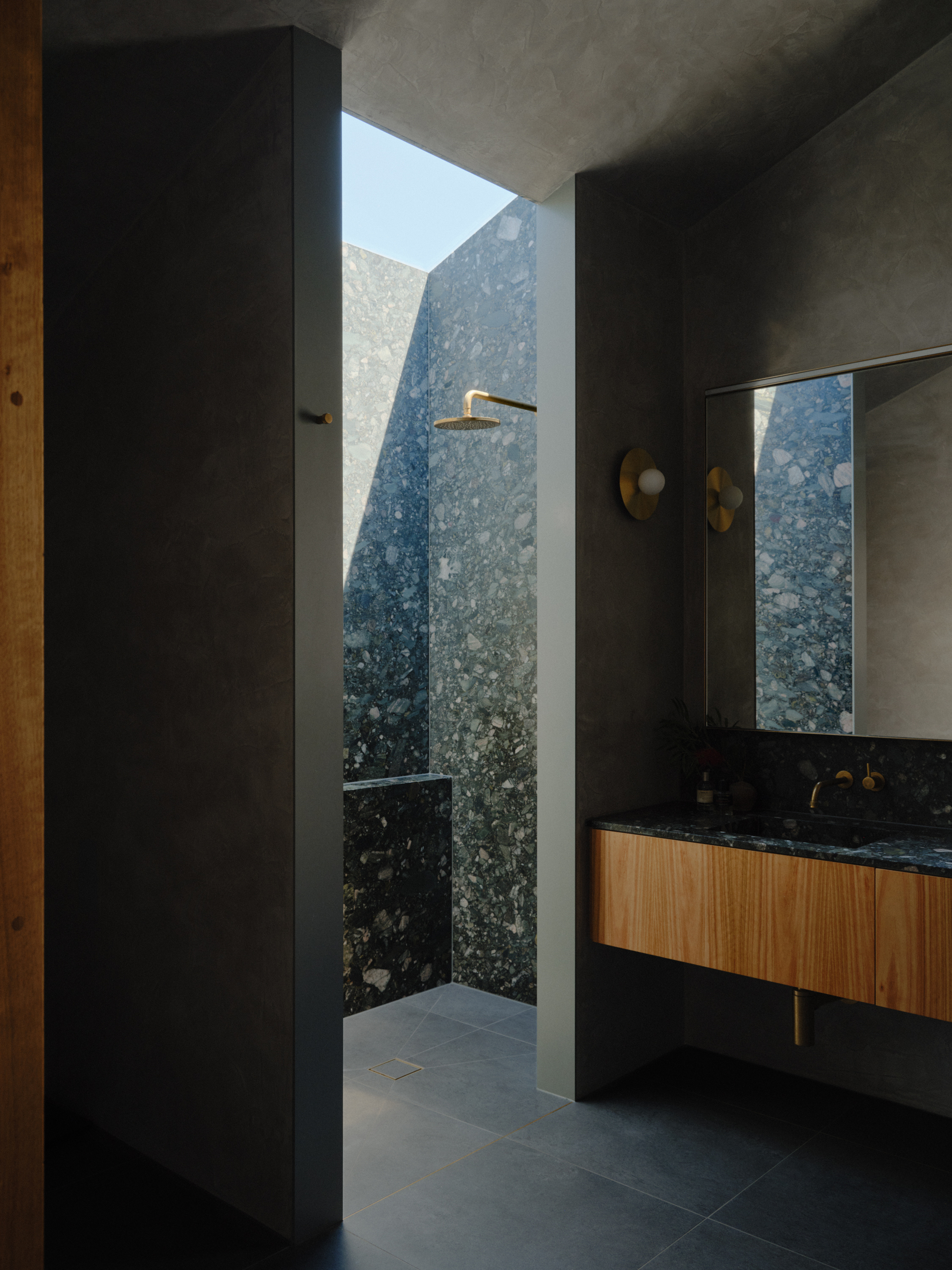 Open shower with speckled stone wall visible through doorway framed by grey concrete