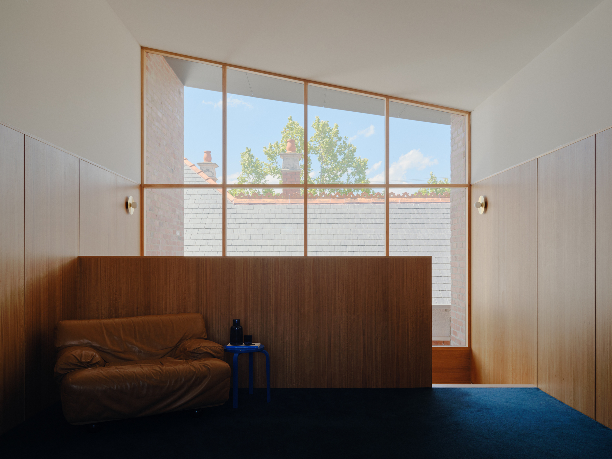 Floor-to-ceiling timber-framed window overlooking courtyard with white brick wall and tree