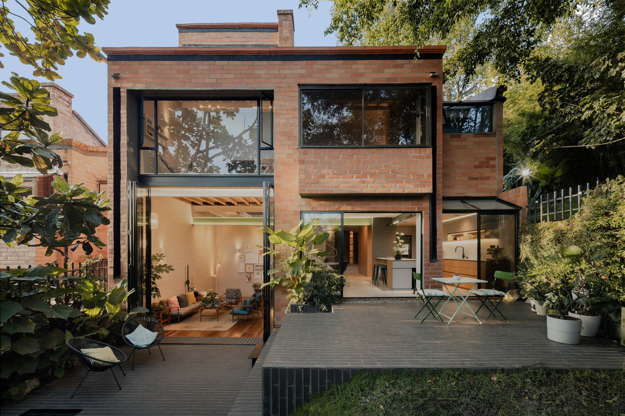 Rear facade with red brick upper volume and glazed ground floor opening to timber deck and garden