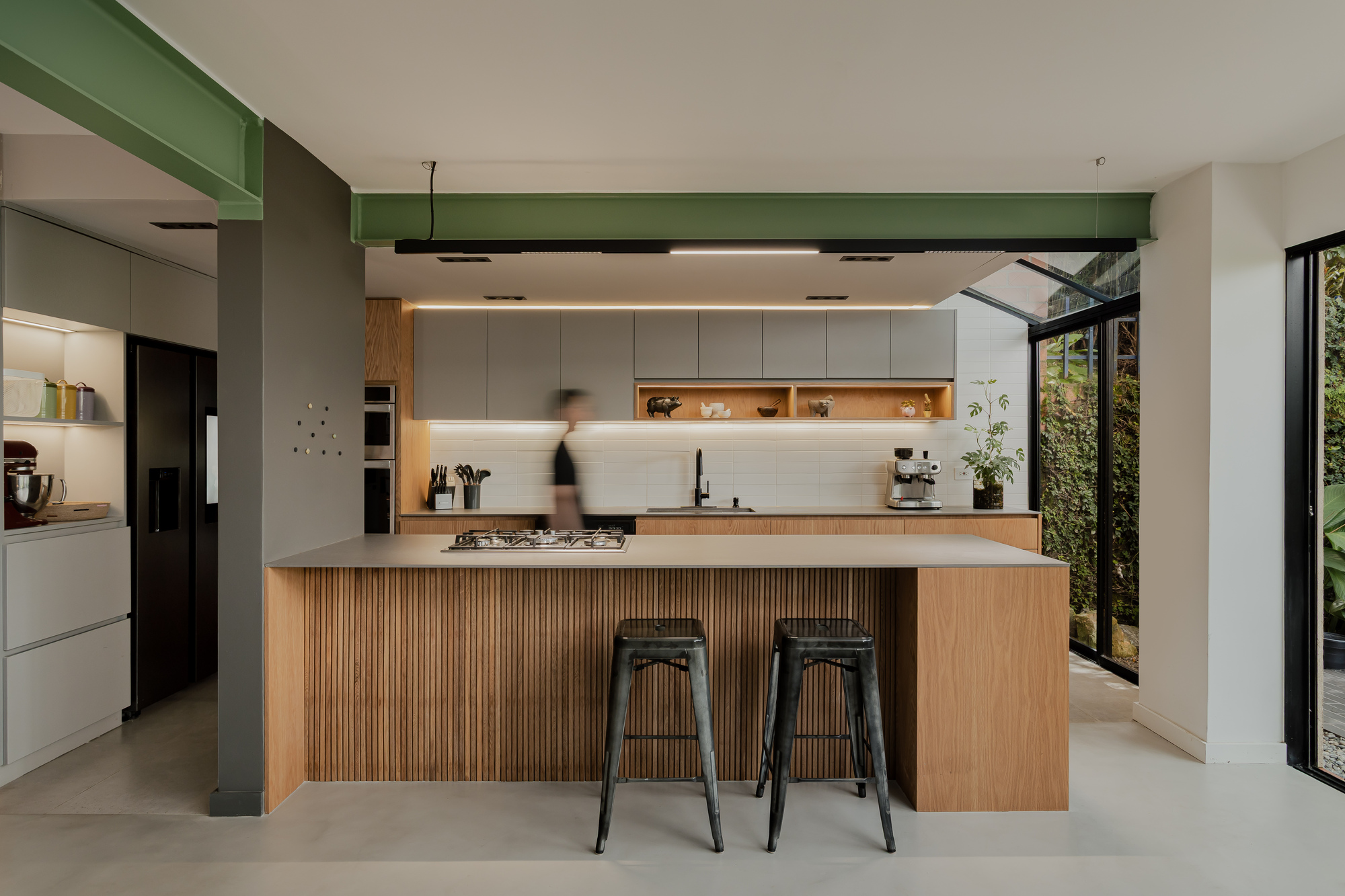 Kitchen island with vertical timber slat cladding beneath green painted beam and pendant lighting