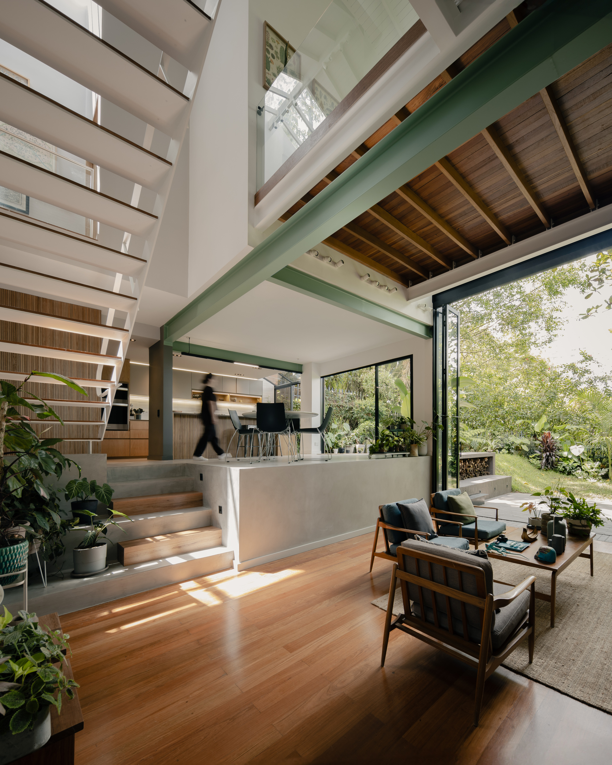 Double-height living space with green structural beams and open timber staircase flooded with natural light