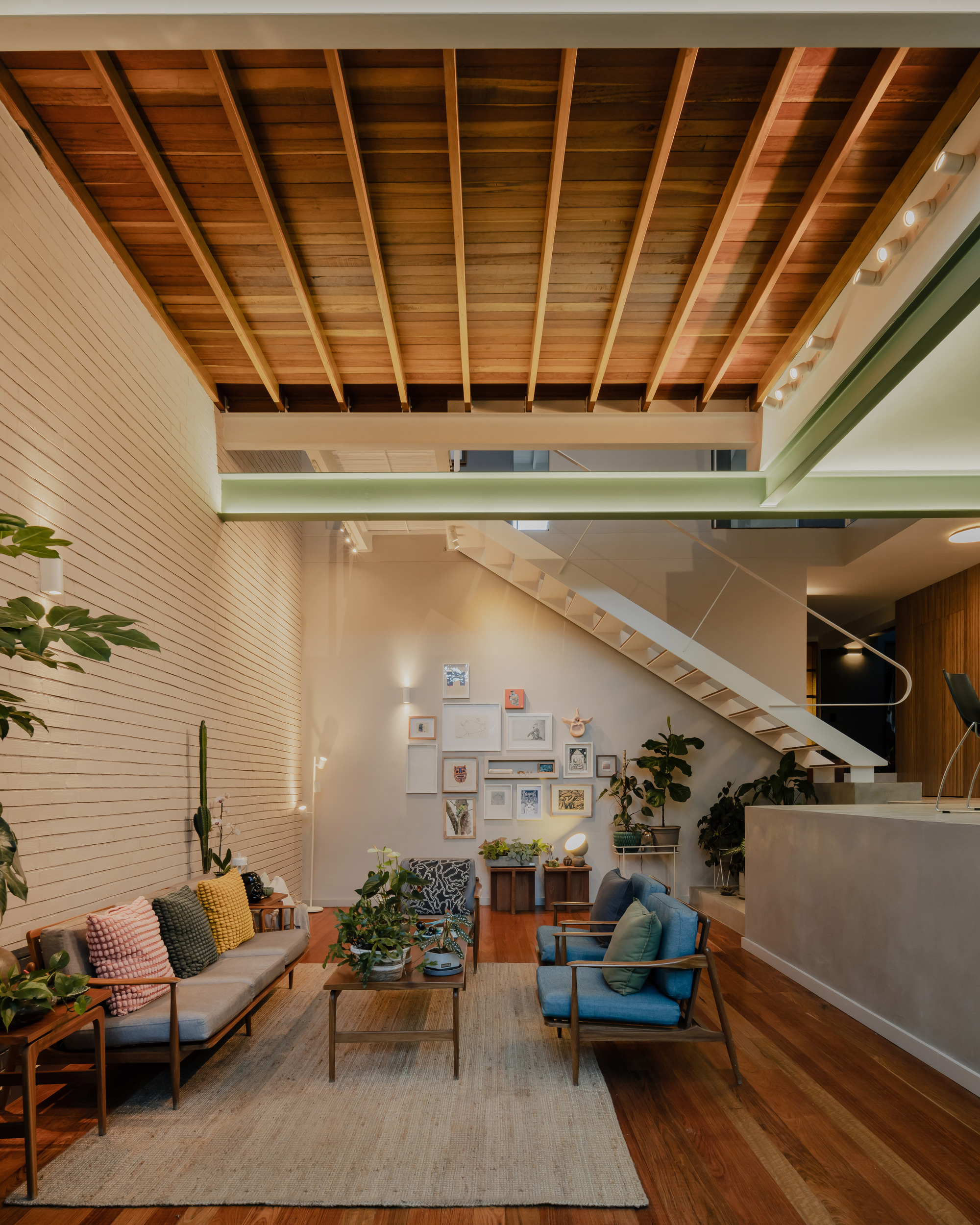 Living area beneath exposed timber ceiling joists with a steel-edged mezzanine and timber stair