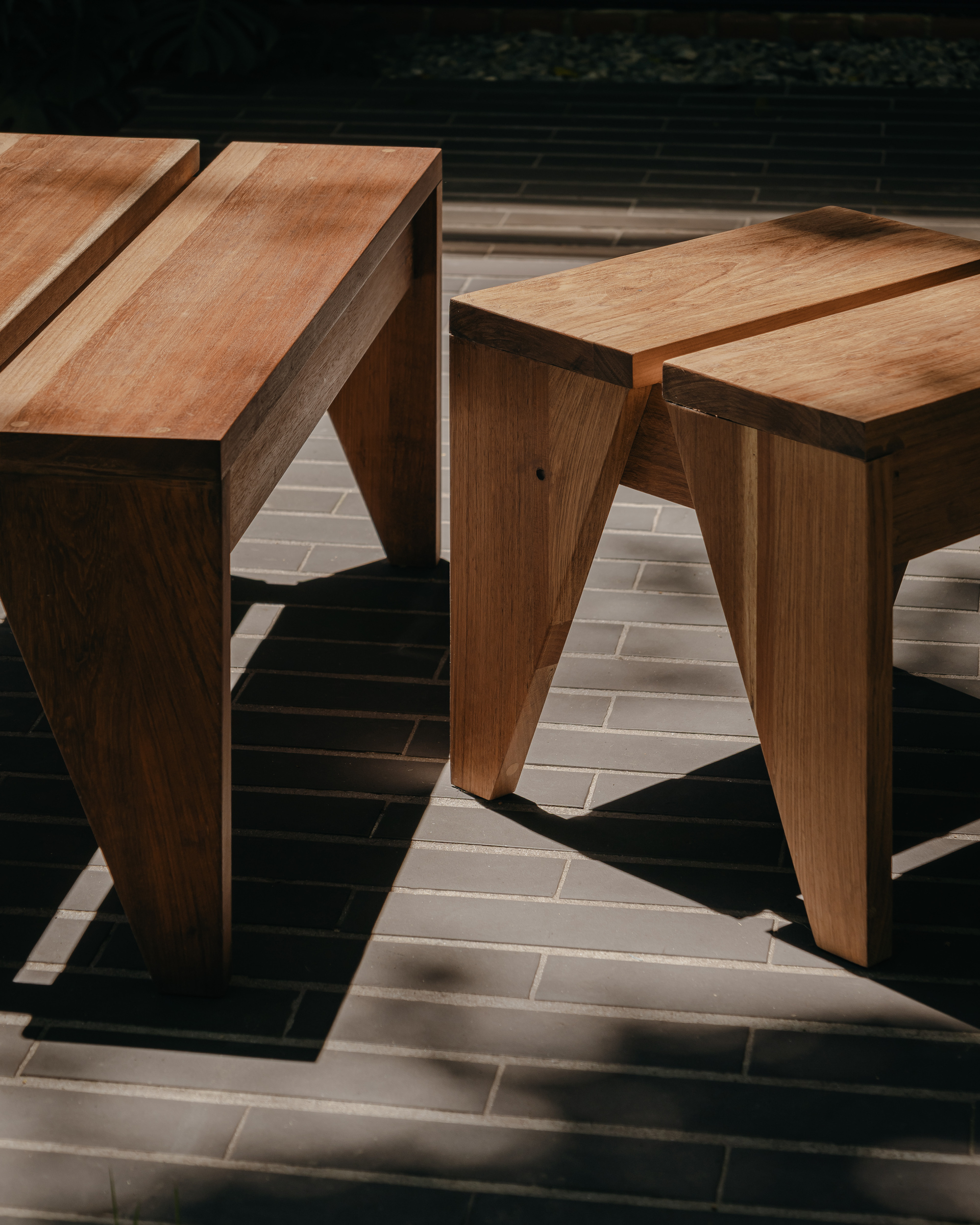 Close-up of angled timber table legs casting shadows on a cream brick paved surface