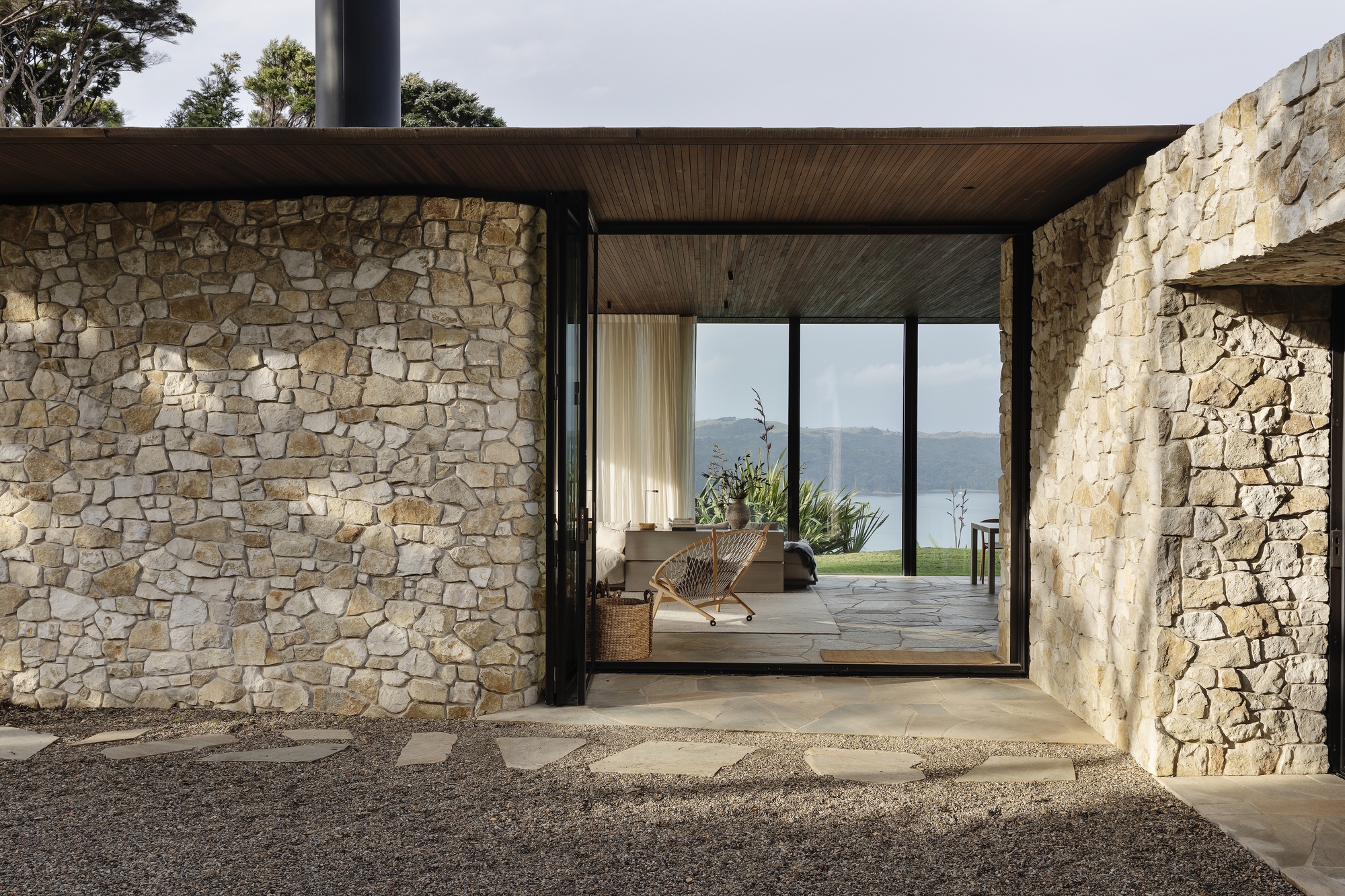 Covered entry breezeway with irregular stone walls and timber ceiling framing a view to distant water