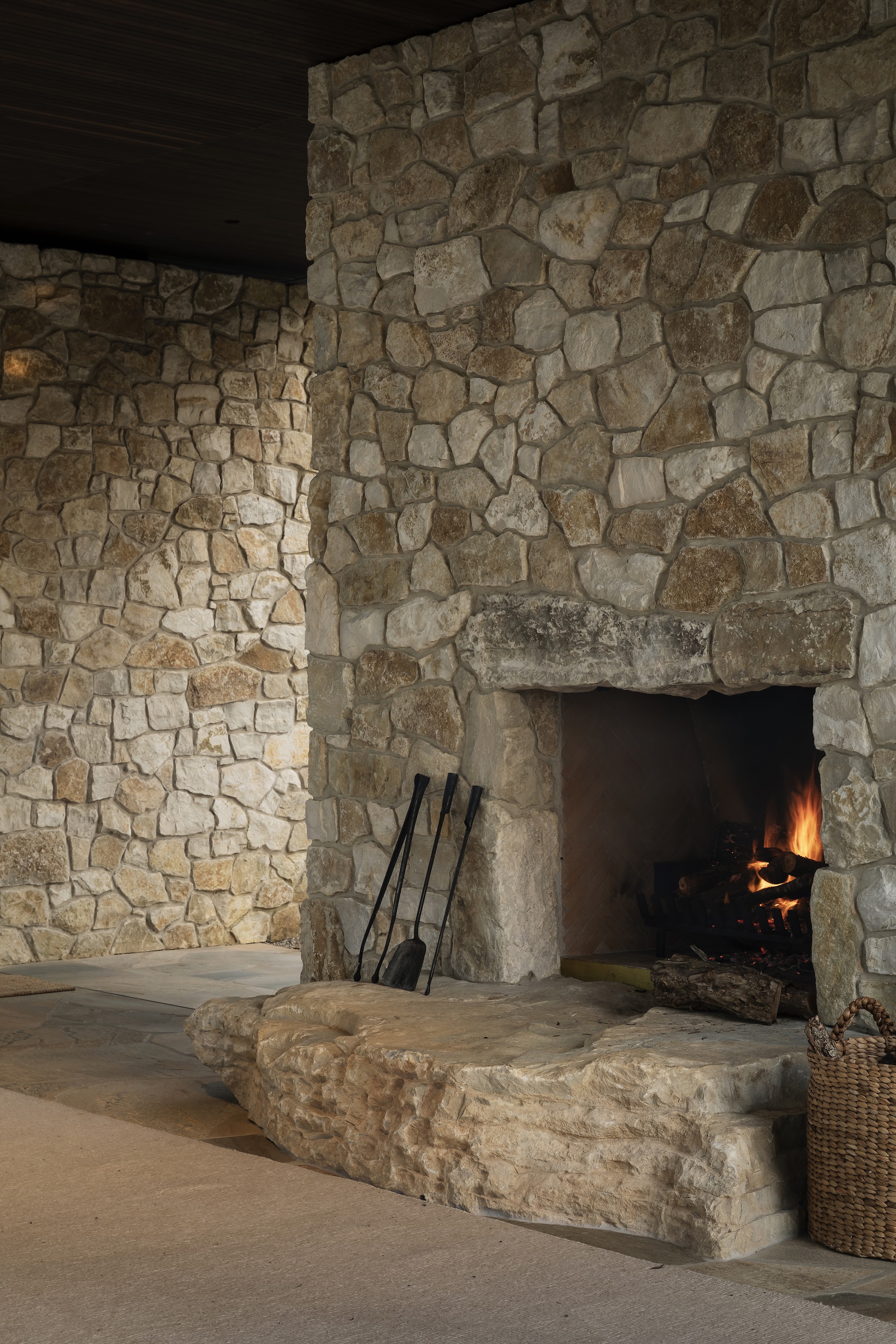 Irregular stone fireplace with active fire and raised stone hearth platform in low light