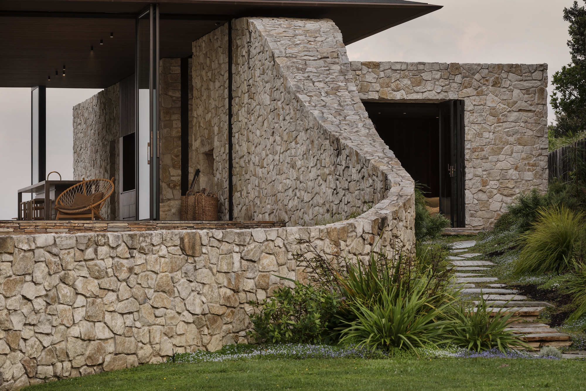 Curved stone retaining wall and exterior staircase beside a paved garden path with ornamental grasses