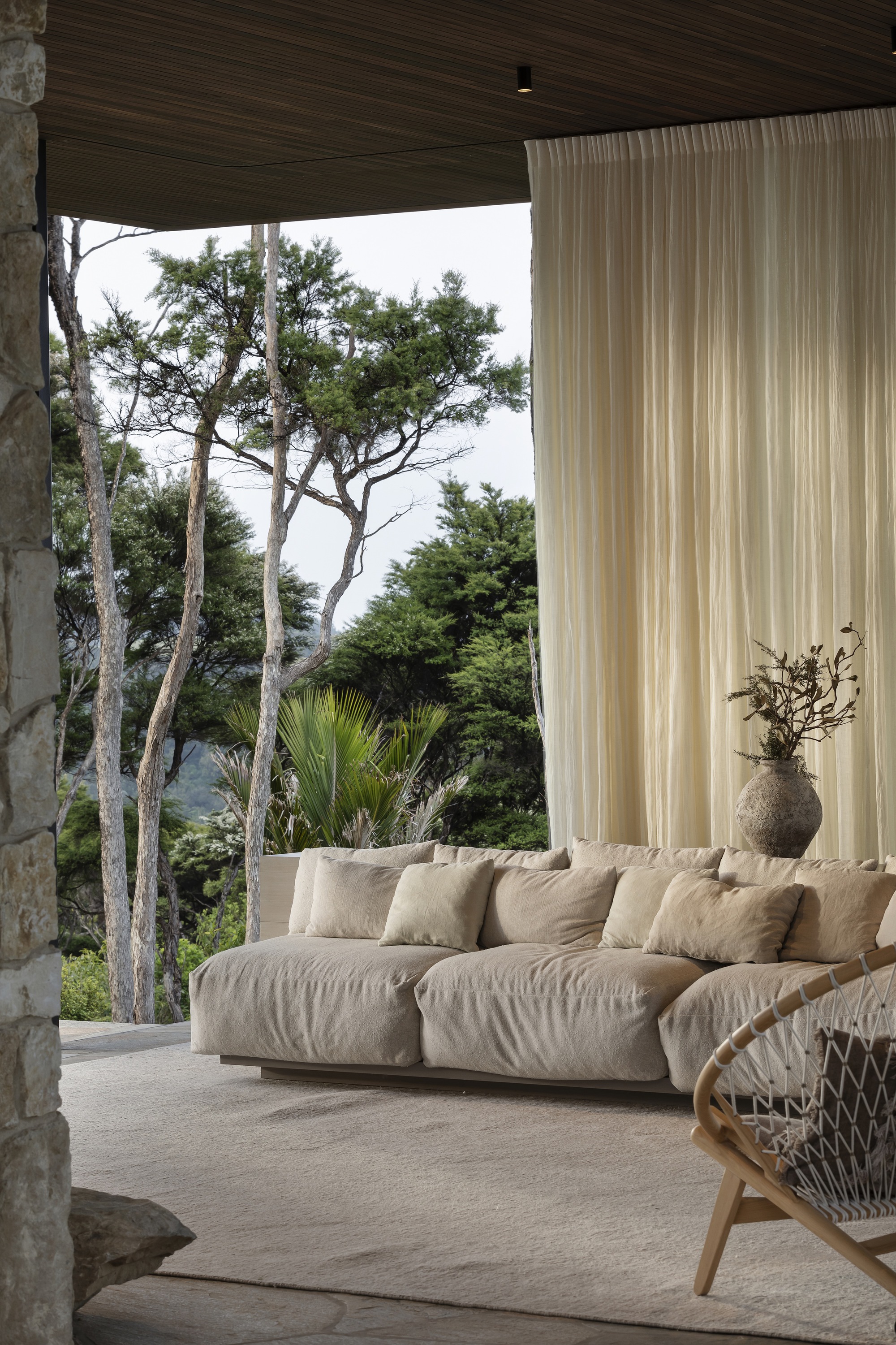 Covered terrace with timber ceiling opening to native trees and coastal vegetation beyond