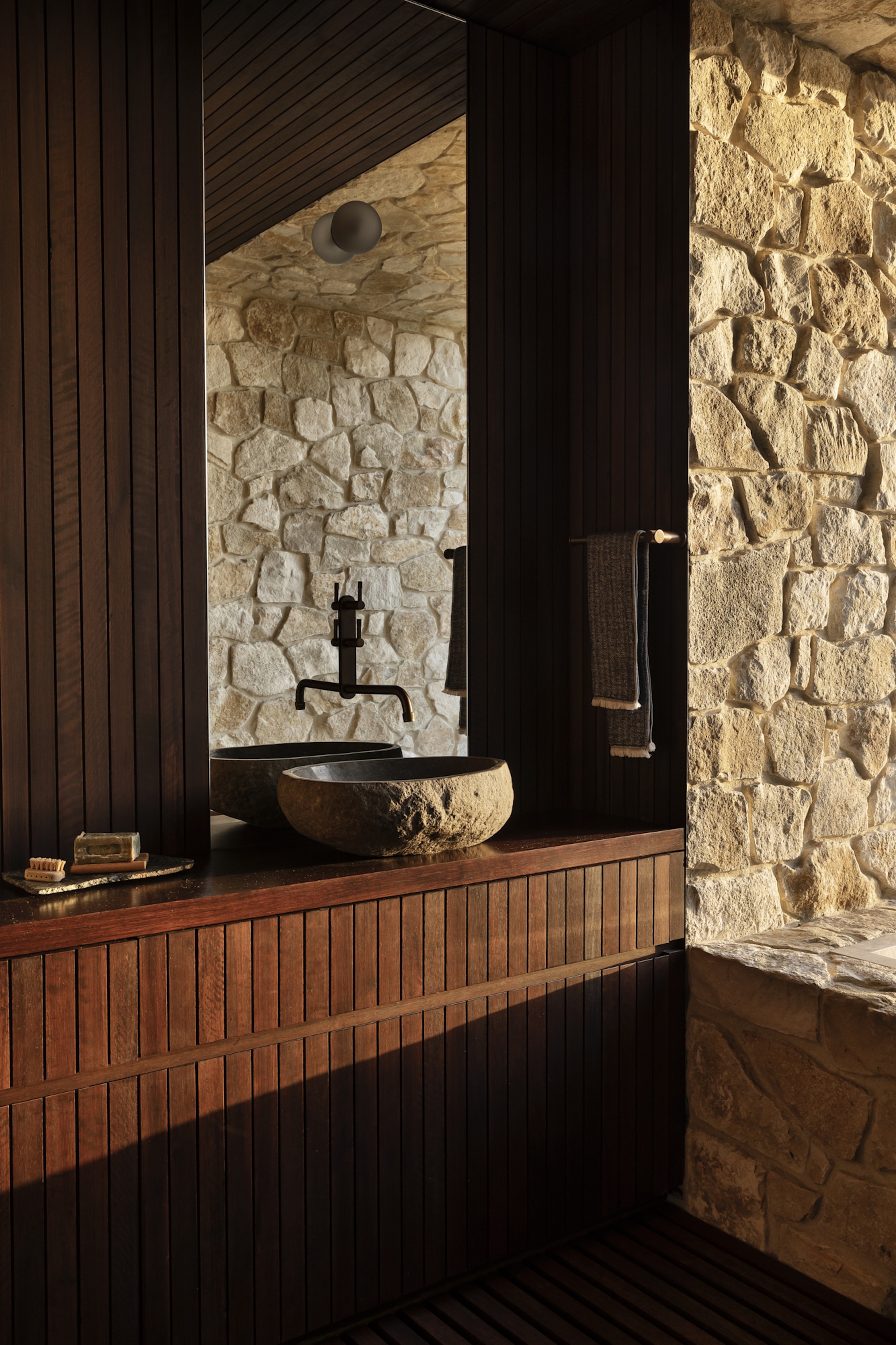 Bathroom vanity with timber slat cabinetry and stone vessel sink against coursed stone walls