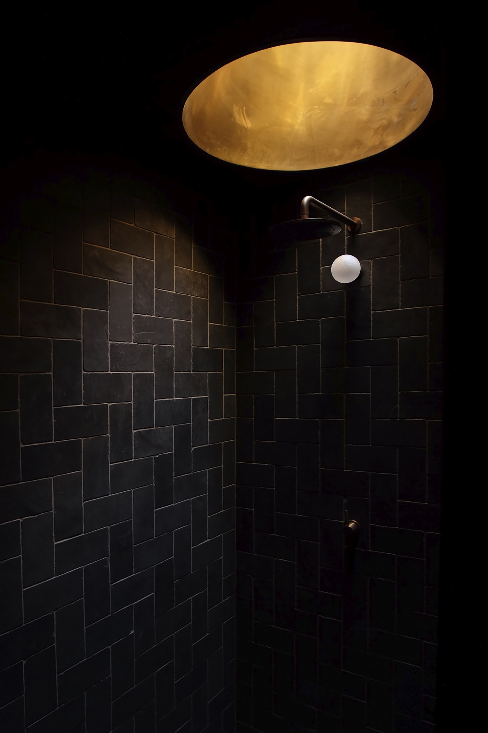 Shower enclosure with black staggered tile walls illuminated by backlit onyx skylight above