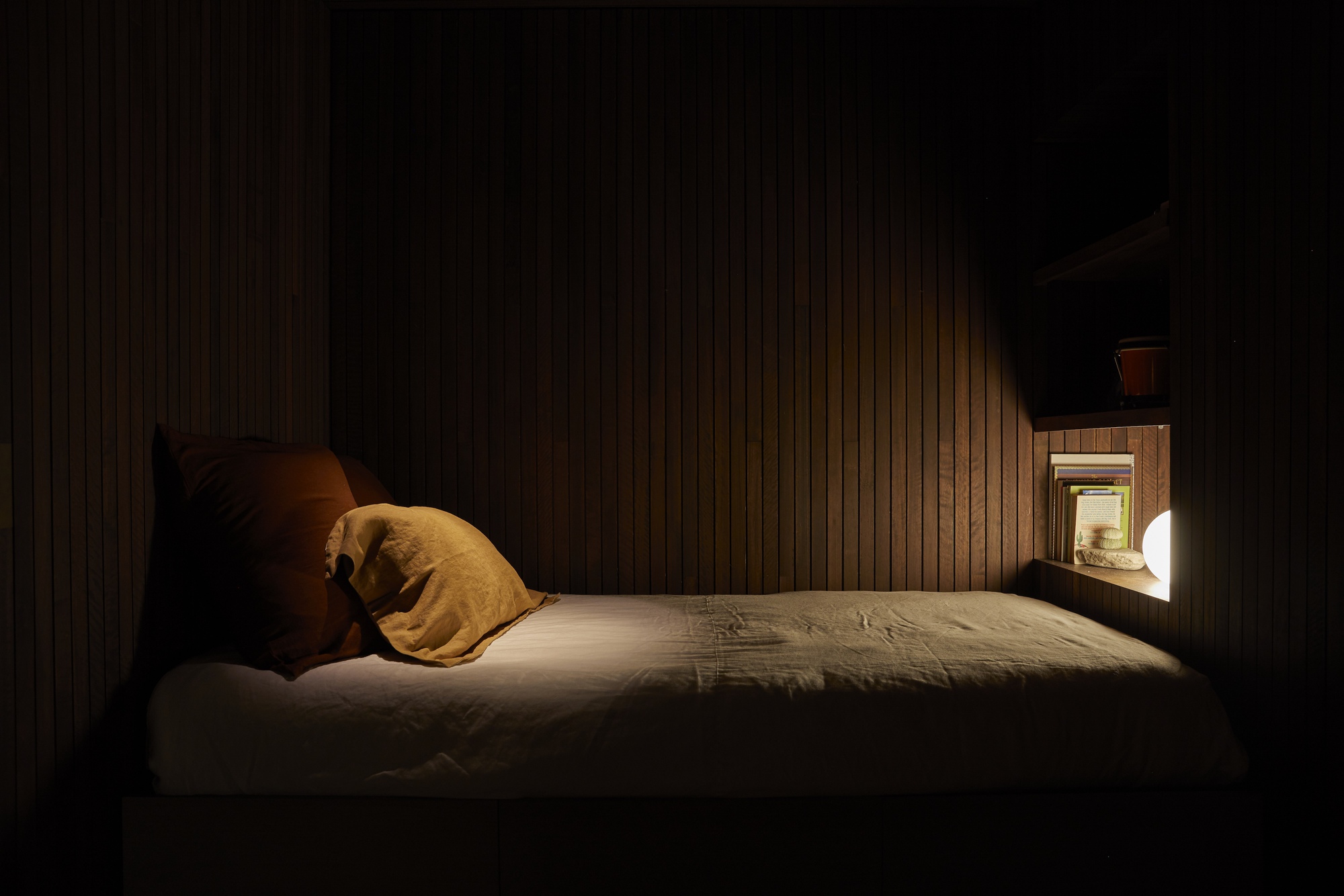Bedroom at night with vertical timber wall cladding and a small illuminated window niche