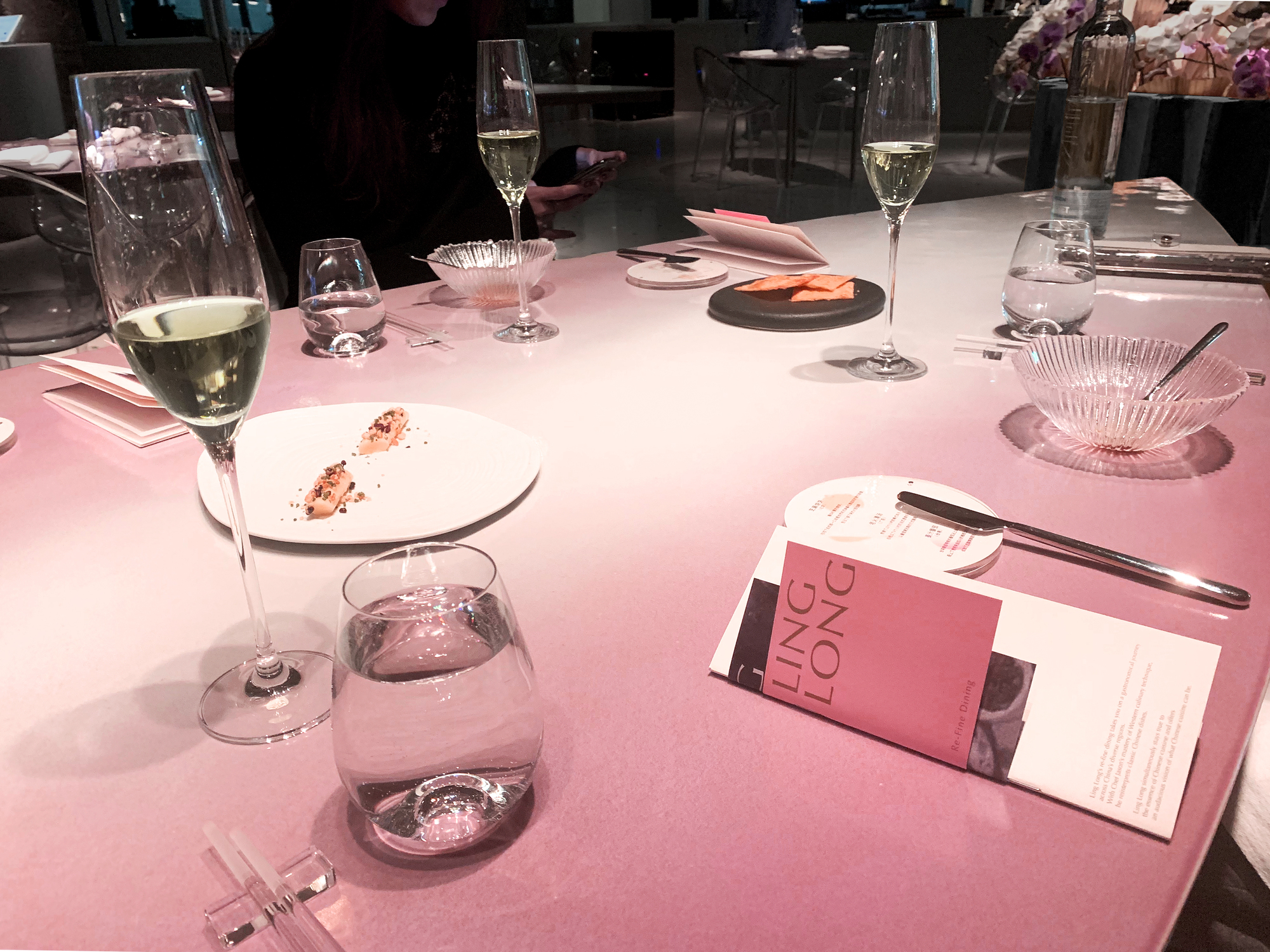 Table detail showing wine glasses, crystal dishes, and pink menu cards on the lacquered surface